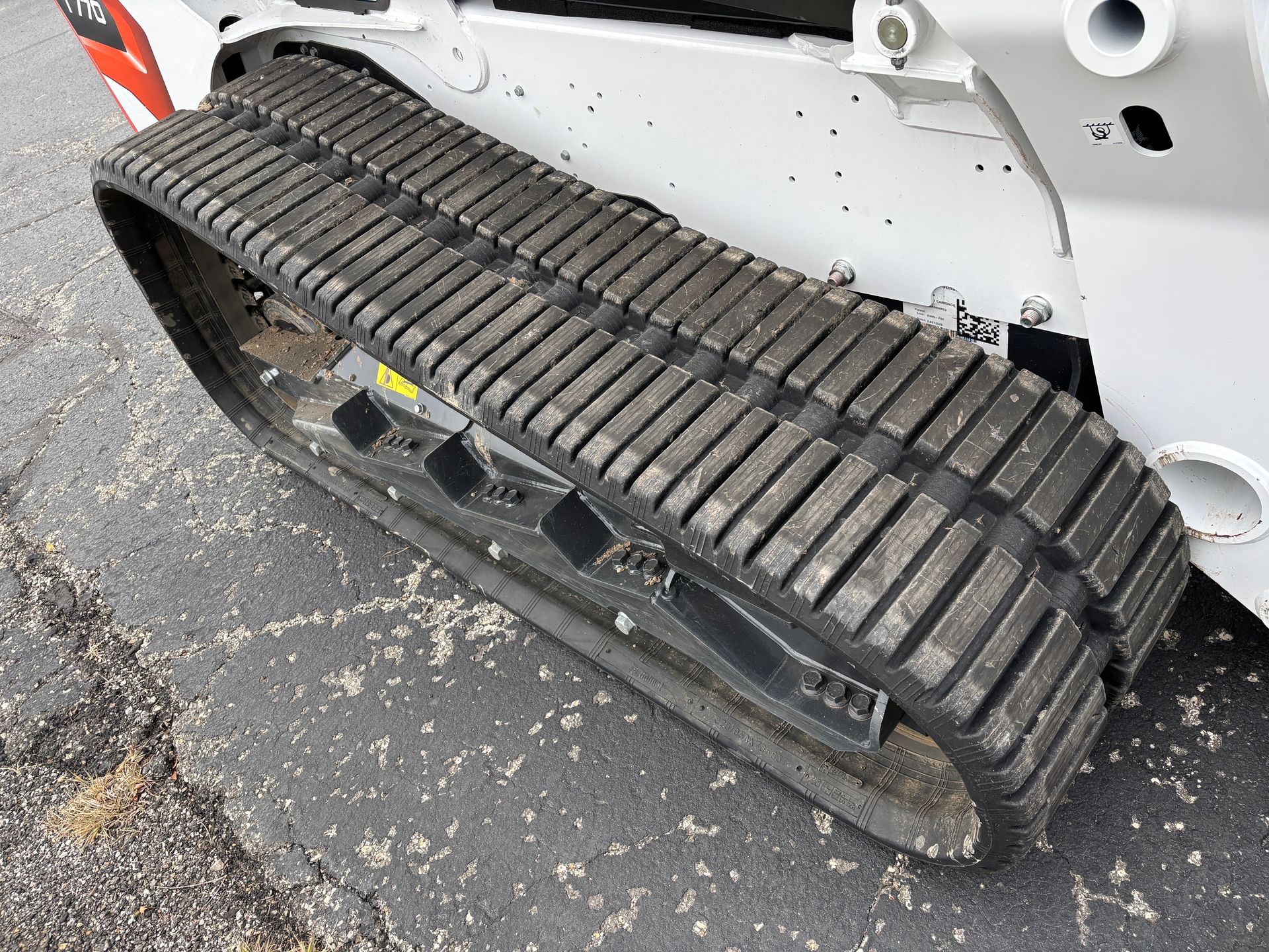 White and black Bobcat compact track loader, close up of tracks, outdoors on pavement, 
