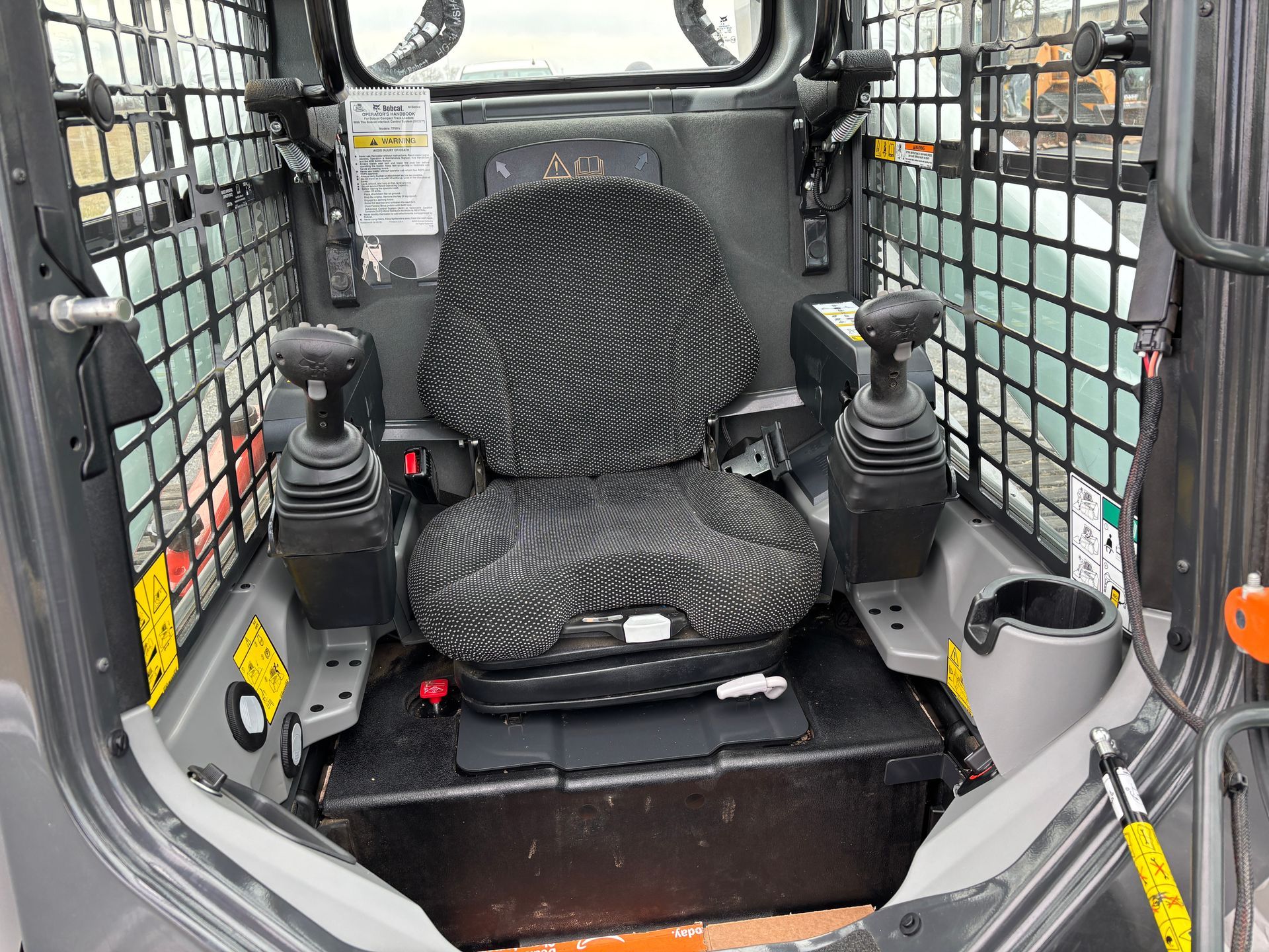 Interior view of a compact track loader cab with seat, joystick controls, and safety cage.