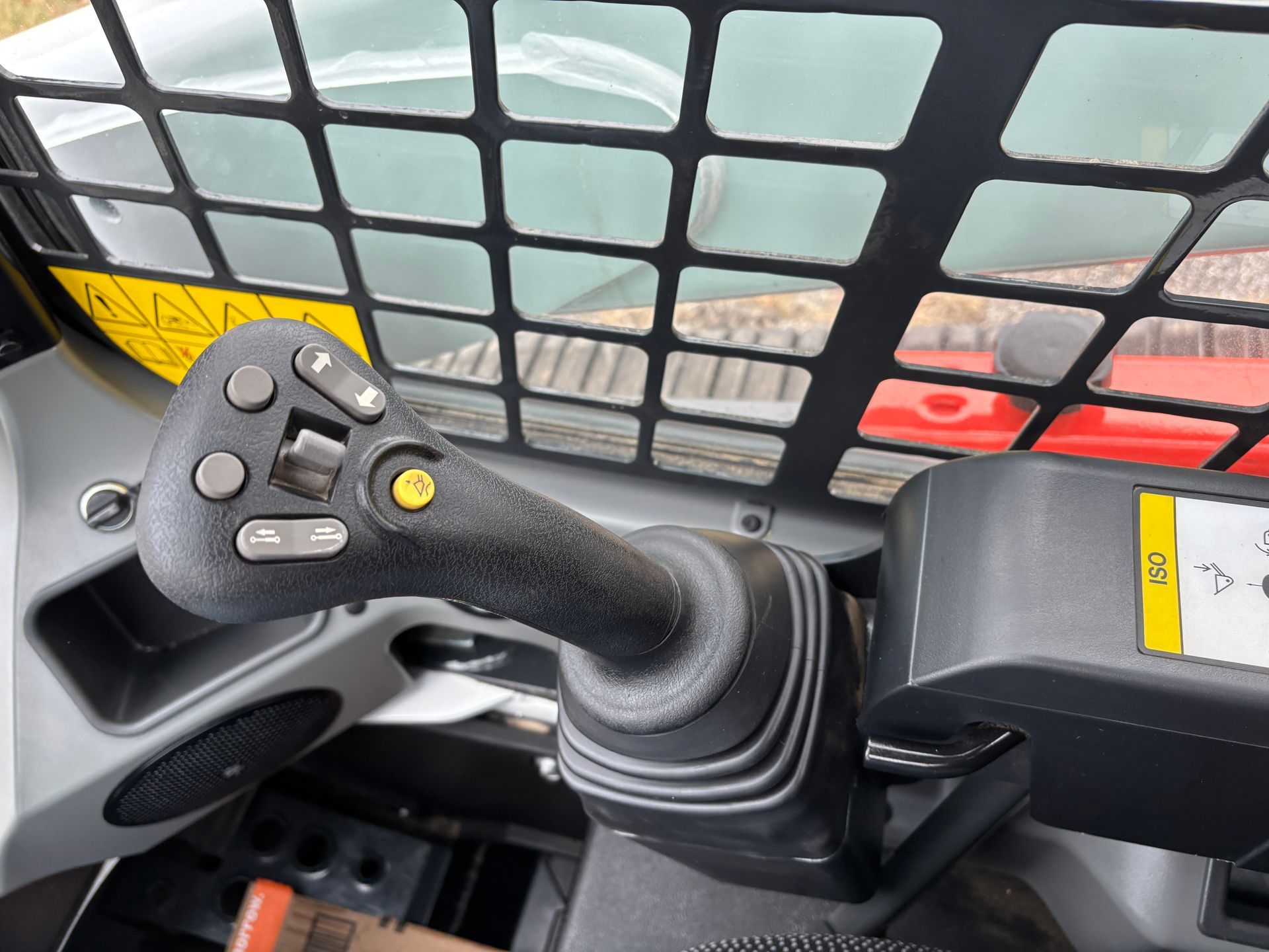 Close-up of a compact track loader joystick with buttons, a safety cage, and warning labels.