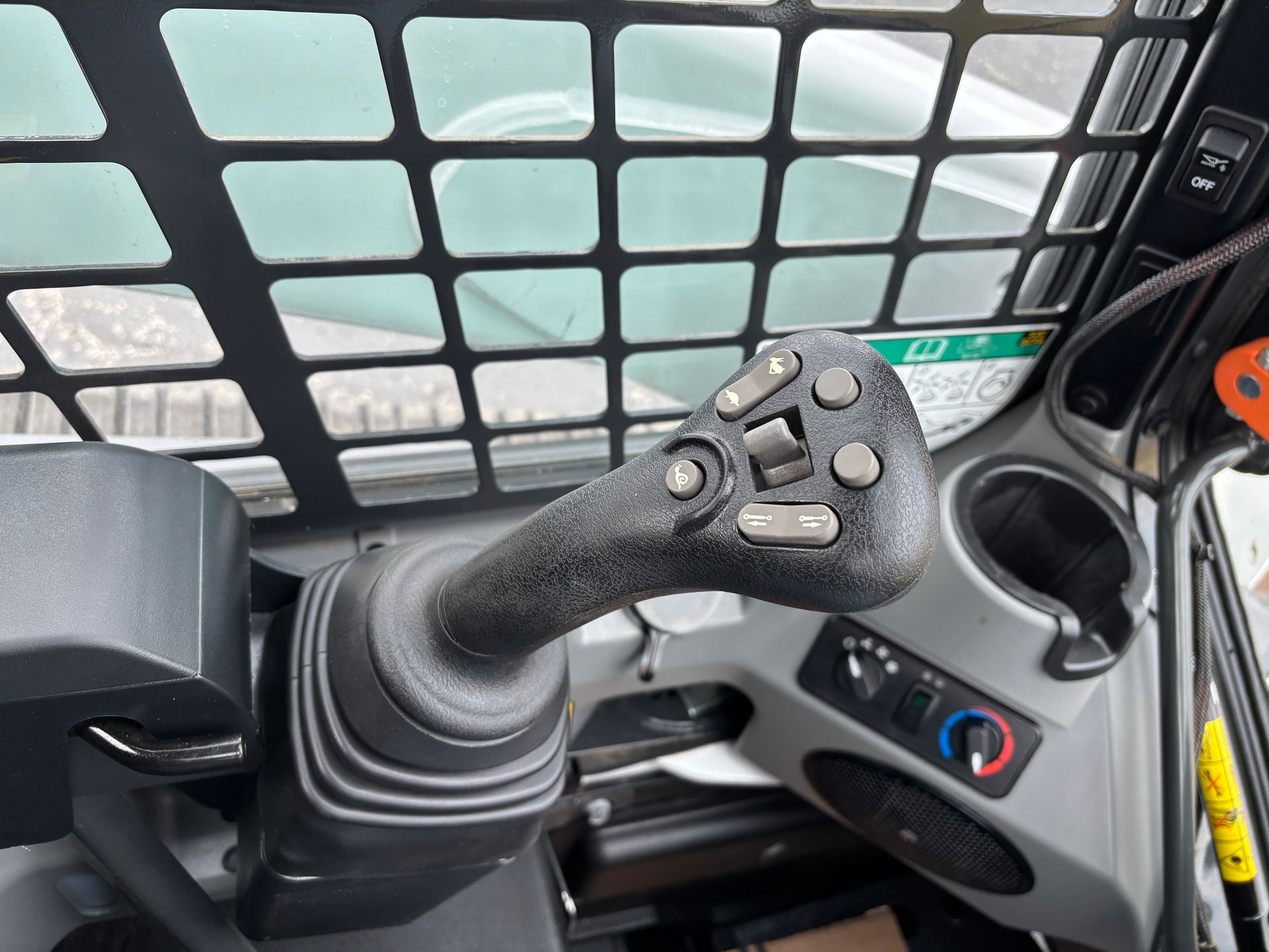 Black control stick in a Bobcat compact track loader cabin. Cup holder and climate control buttons visible.