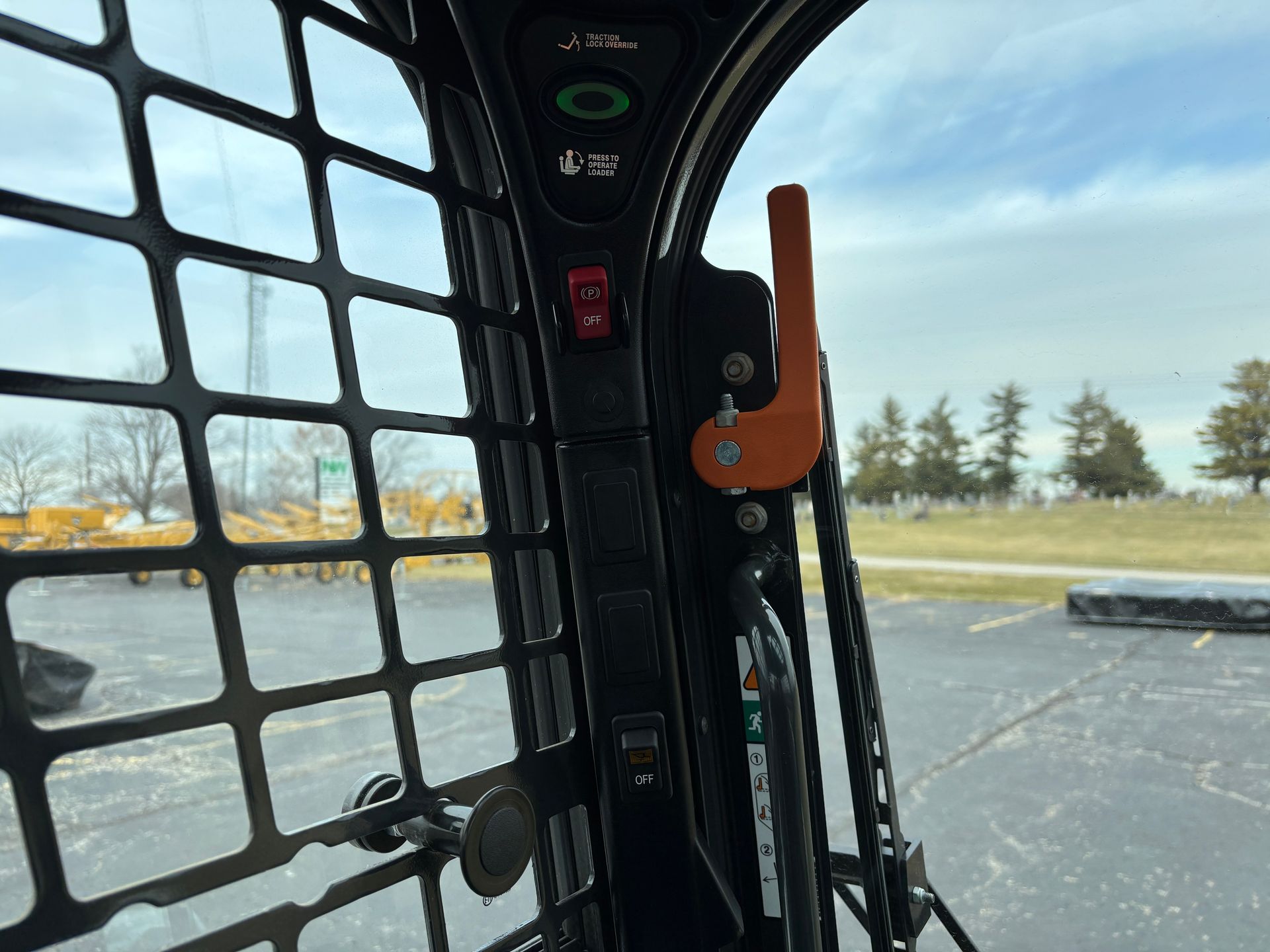 Interior of a compact track loader cab with controls, including an orange lever and a red switch.