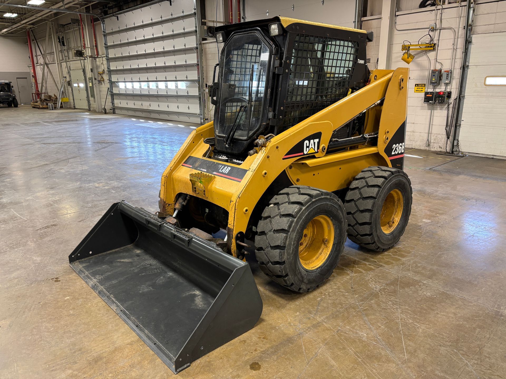 Yellow Caterpillar skid steer loader with bucket indoors.