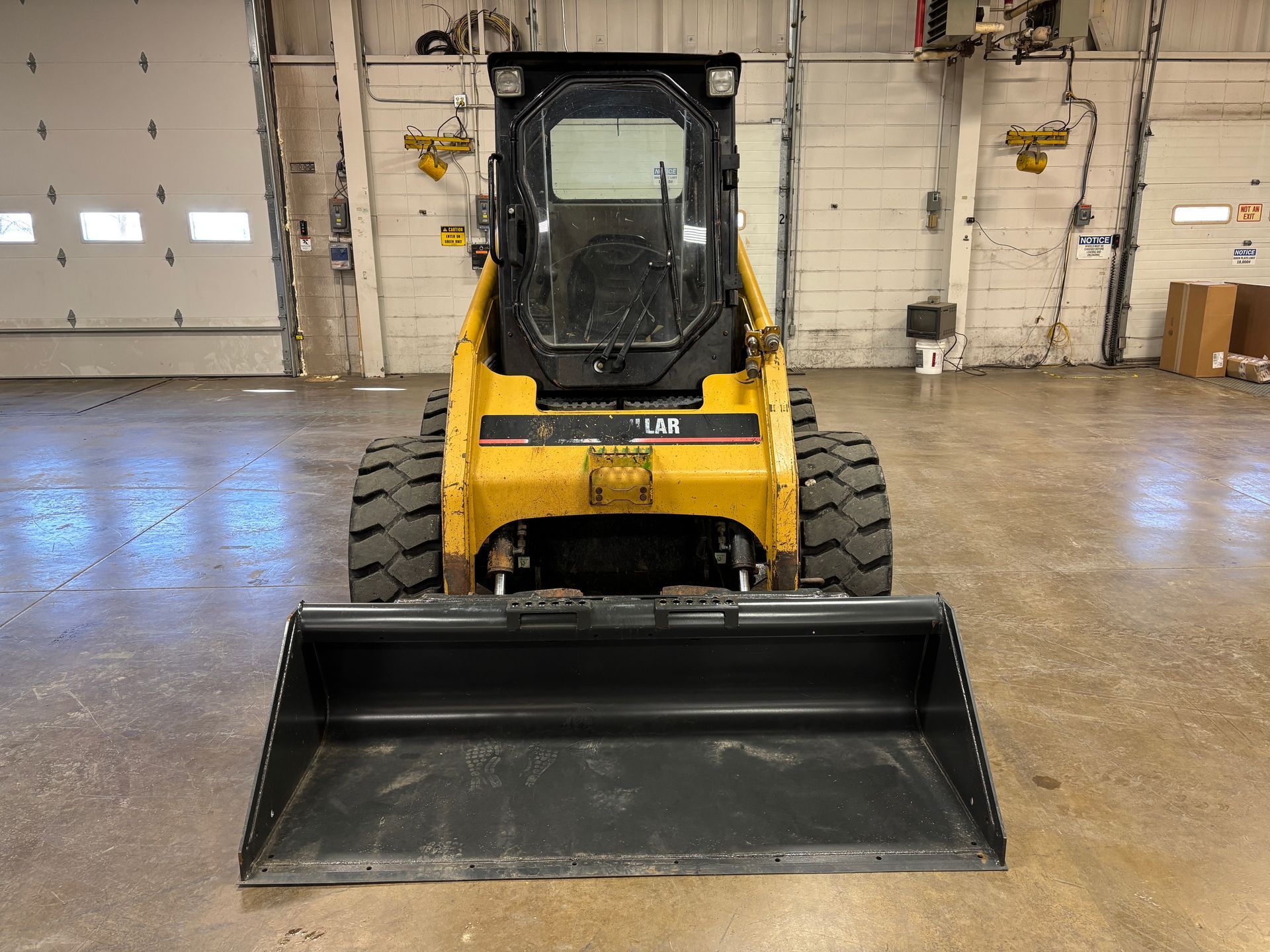Yellow Caterpillar skid steer with black bucket, inside a warehouse.