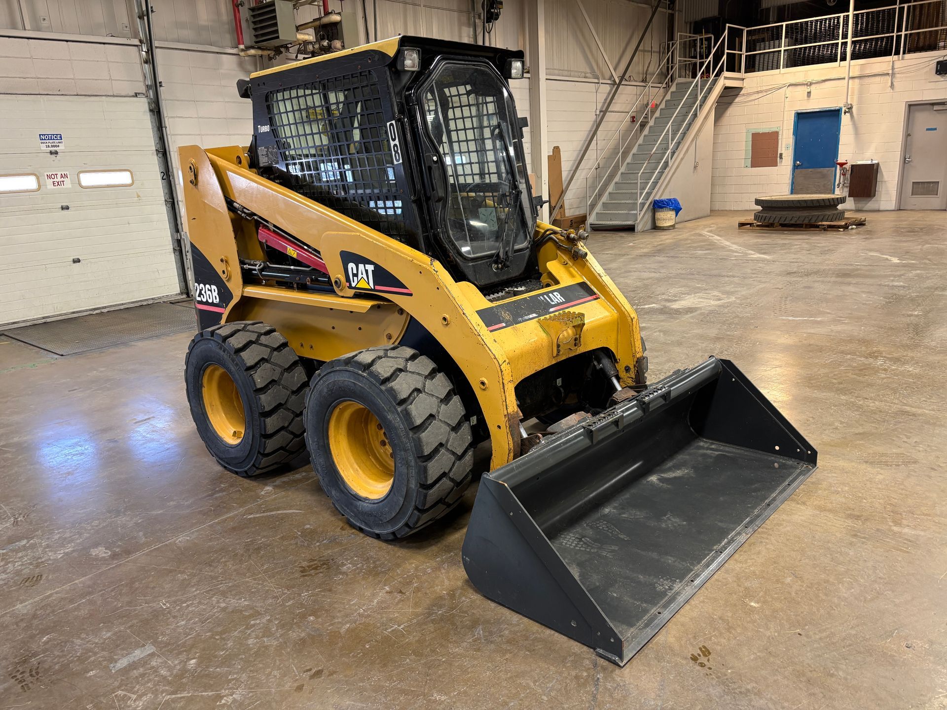 Yellow Caterpillar skid steer loader with bucket in a warehouse.