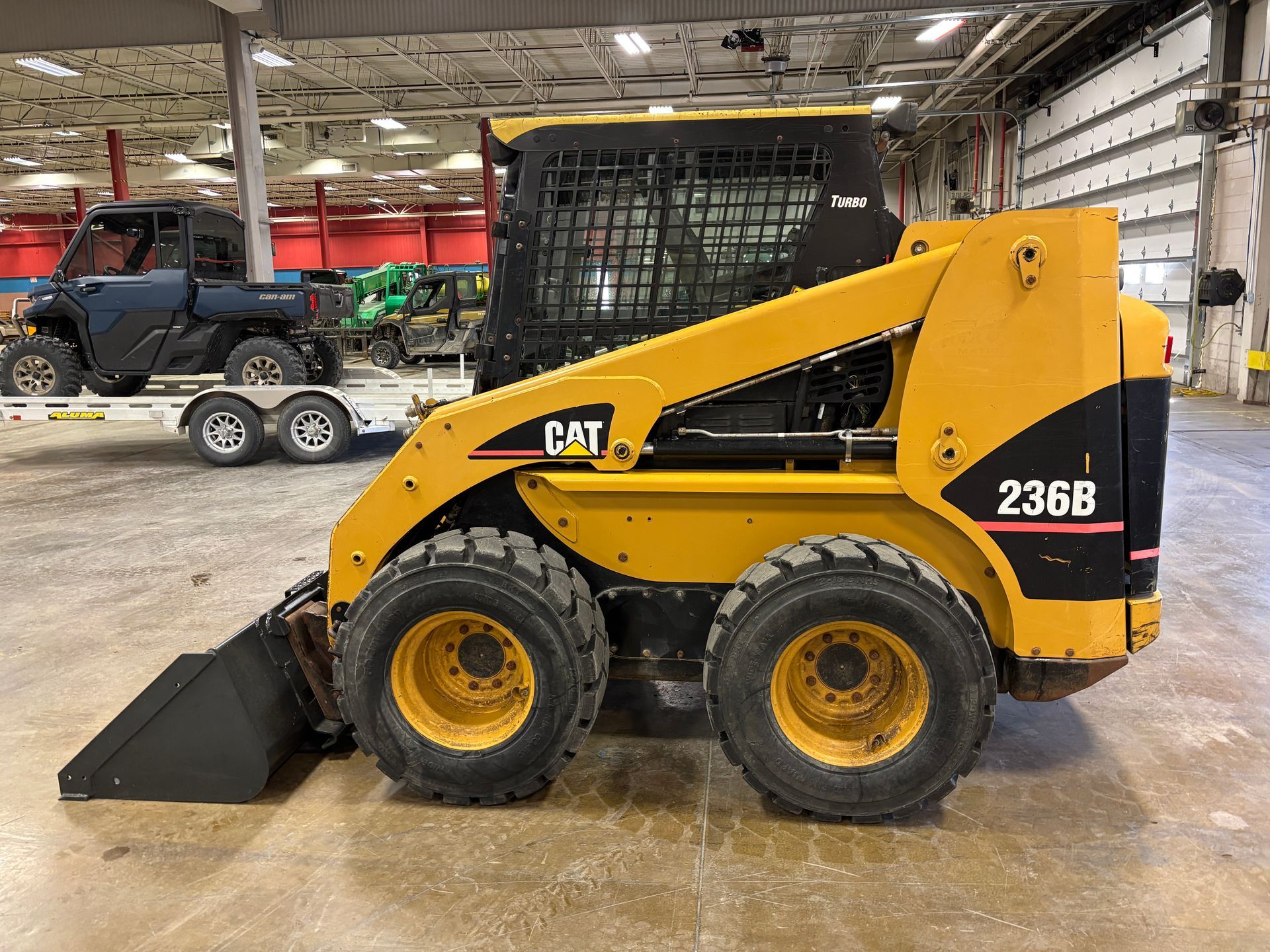 Yellow Caterpillar 236B skid steer loader with a black bucket. Inside a warehouse.