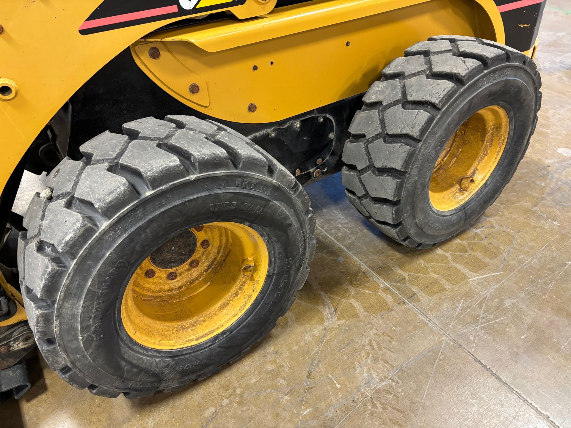 Yellow skid steer tires, showing tread detail, sitting on a light-colored surface.