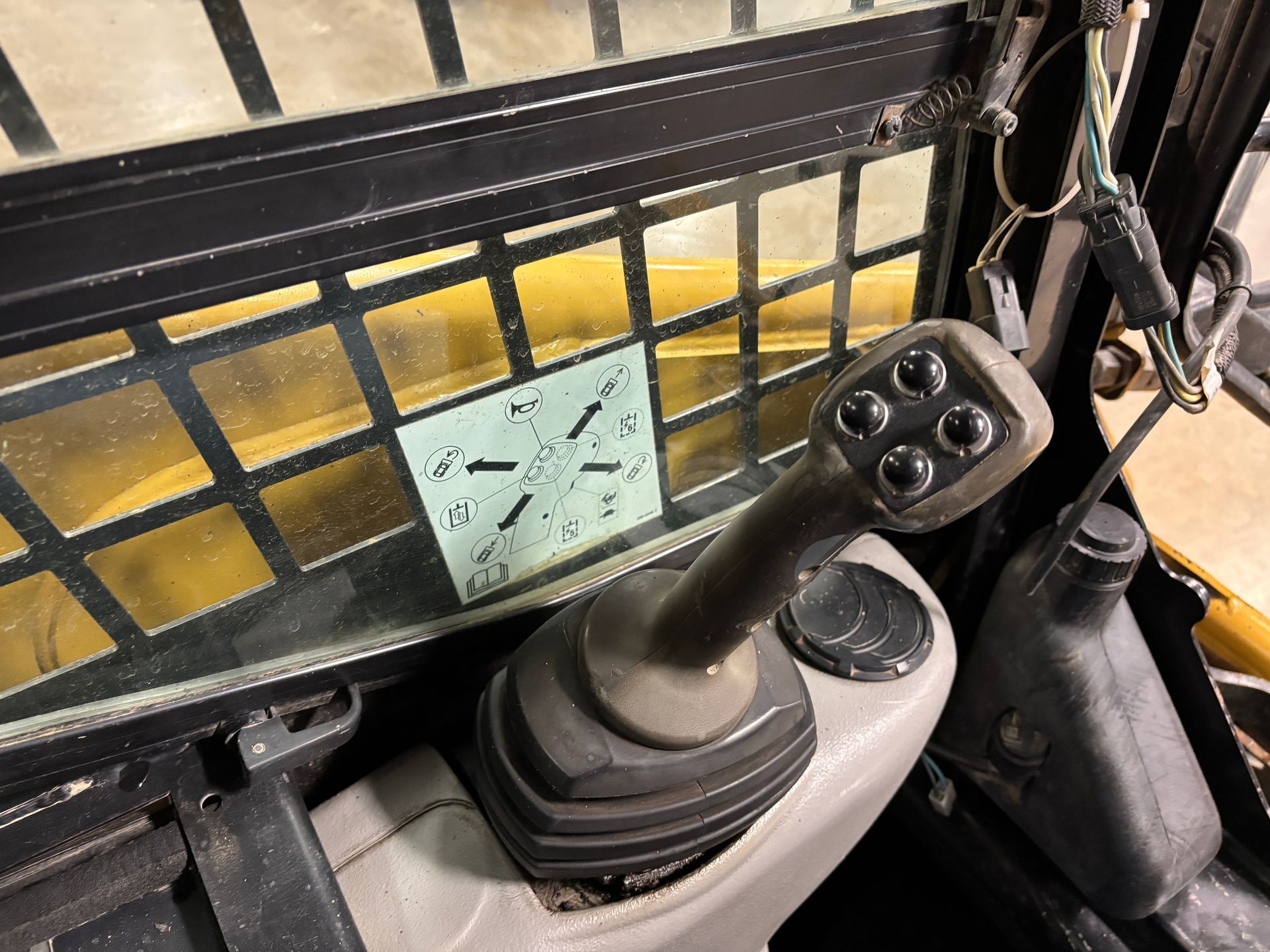 Interior view of a skid steer cab, showing a joystick control with four buttons and a sticker on the glass.