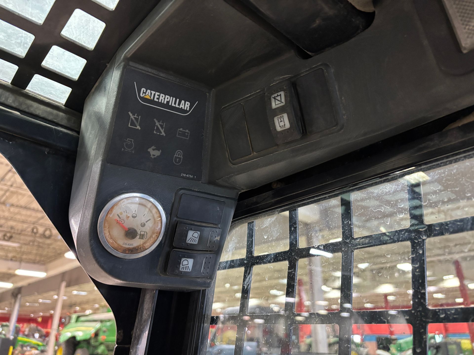 Interior of a Caterpillar skid steer cab showing control panel with buttons, gauges, and the Caterpillar logo.