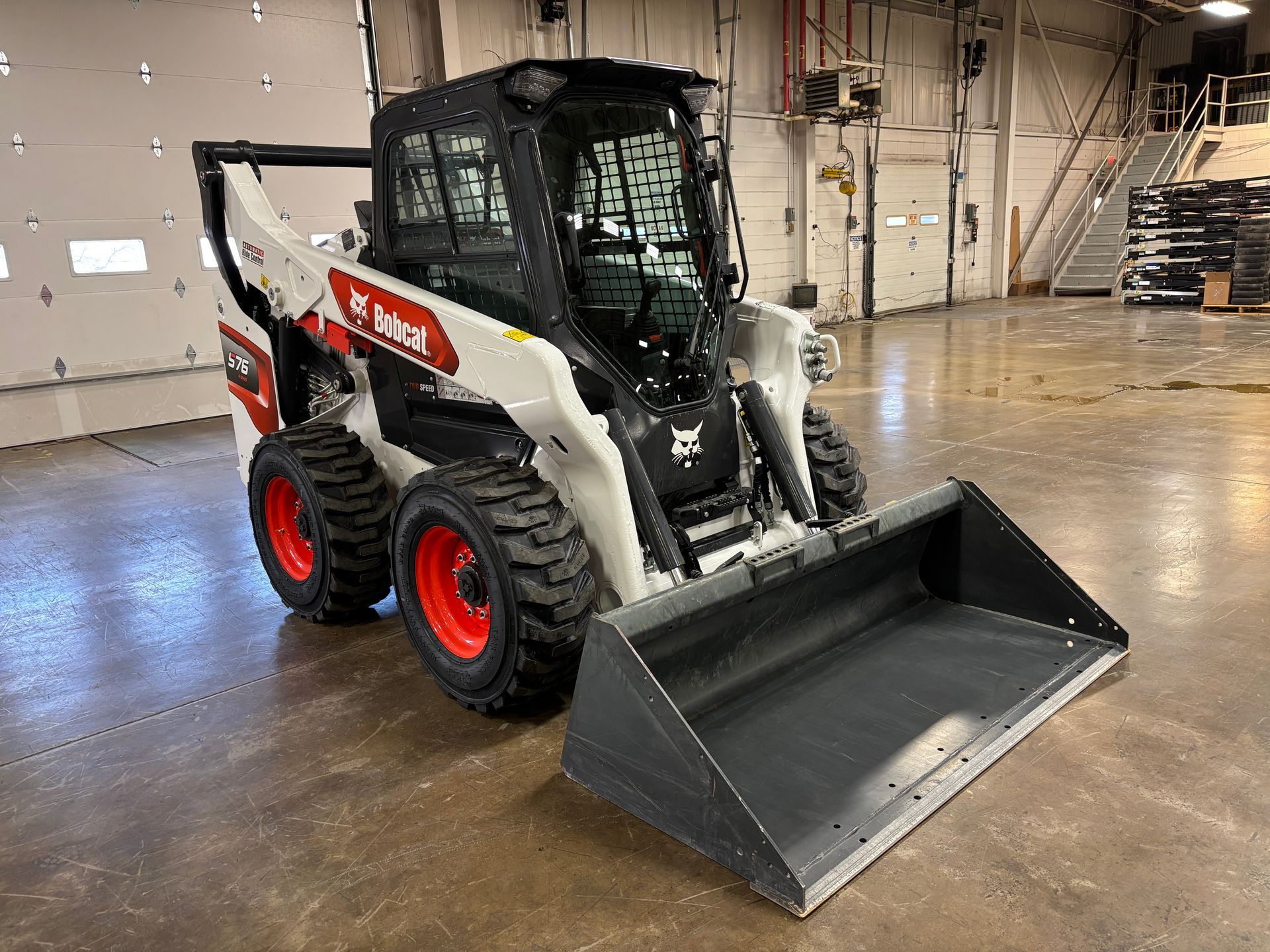White Bobcat skid-steer loader with a black cab and bucket on a concrete floor in a warehouse.