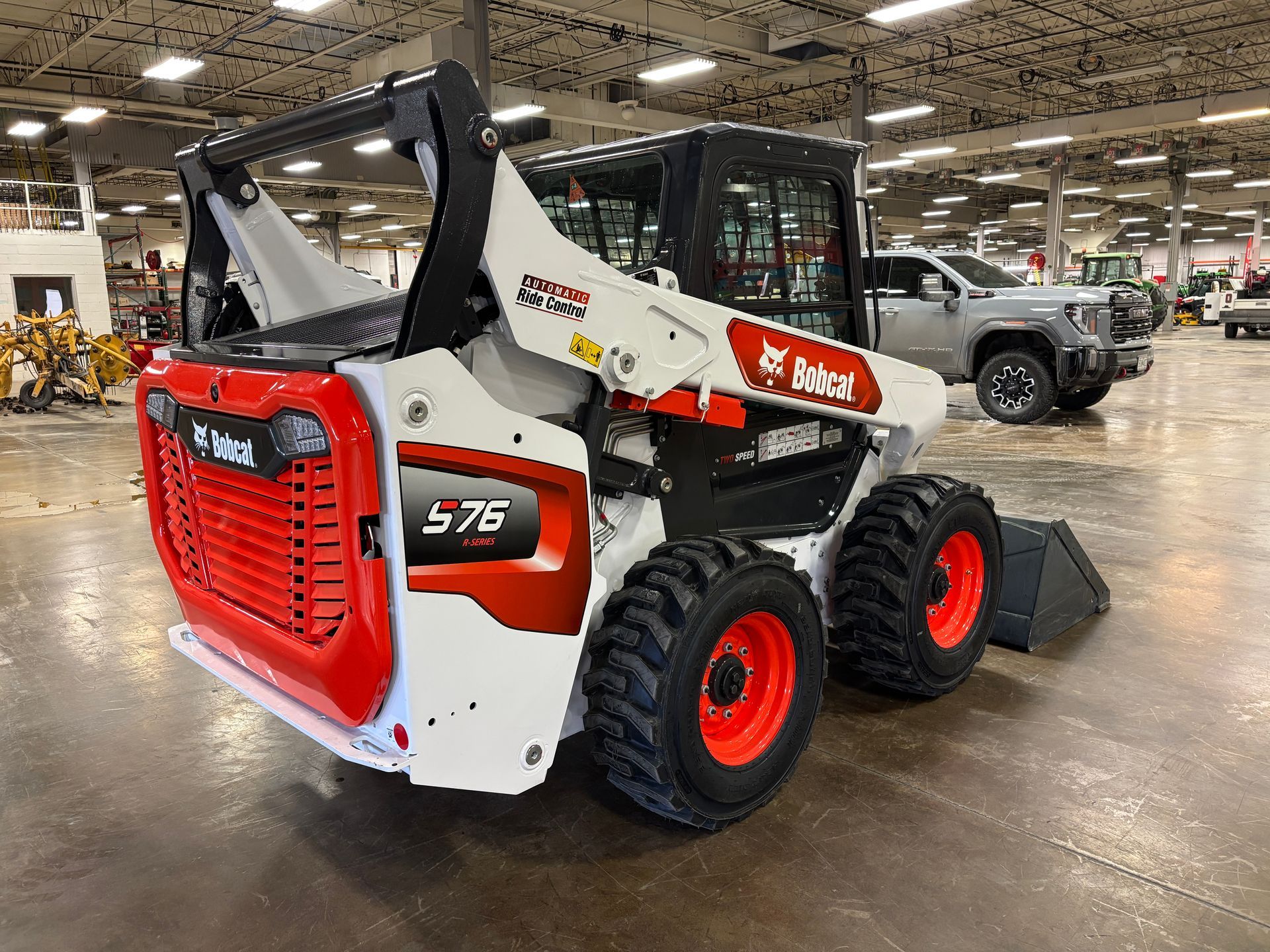 Bobcat S76 skid-steer loader, white and red, in a large warehouse.