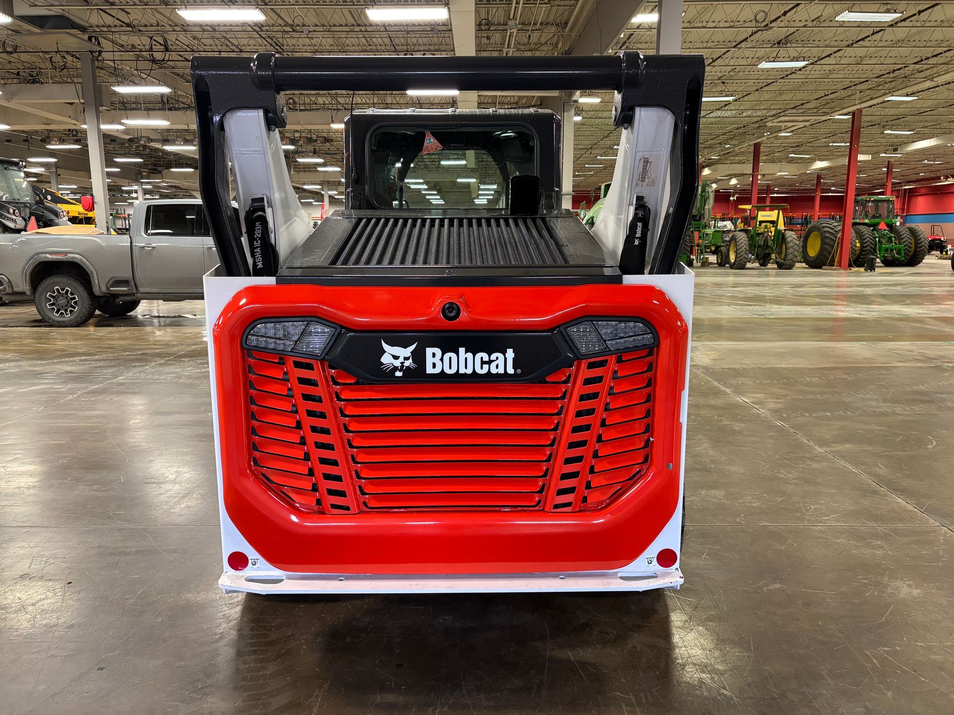 Red and white Bobcat skid-steer loader, rear view. Grille with Bobcat logo, indoors.