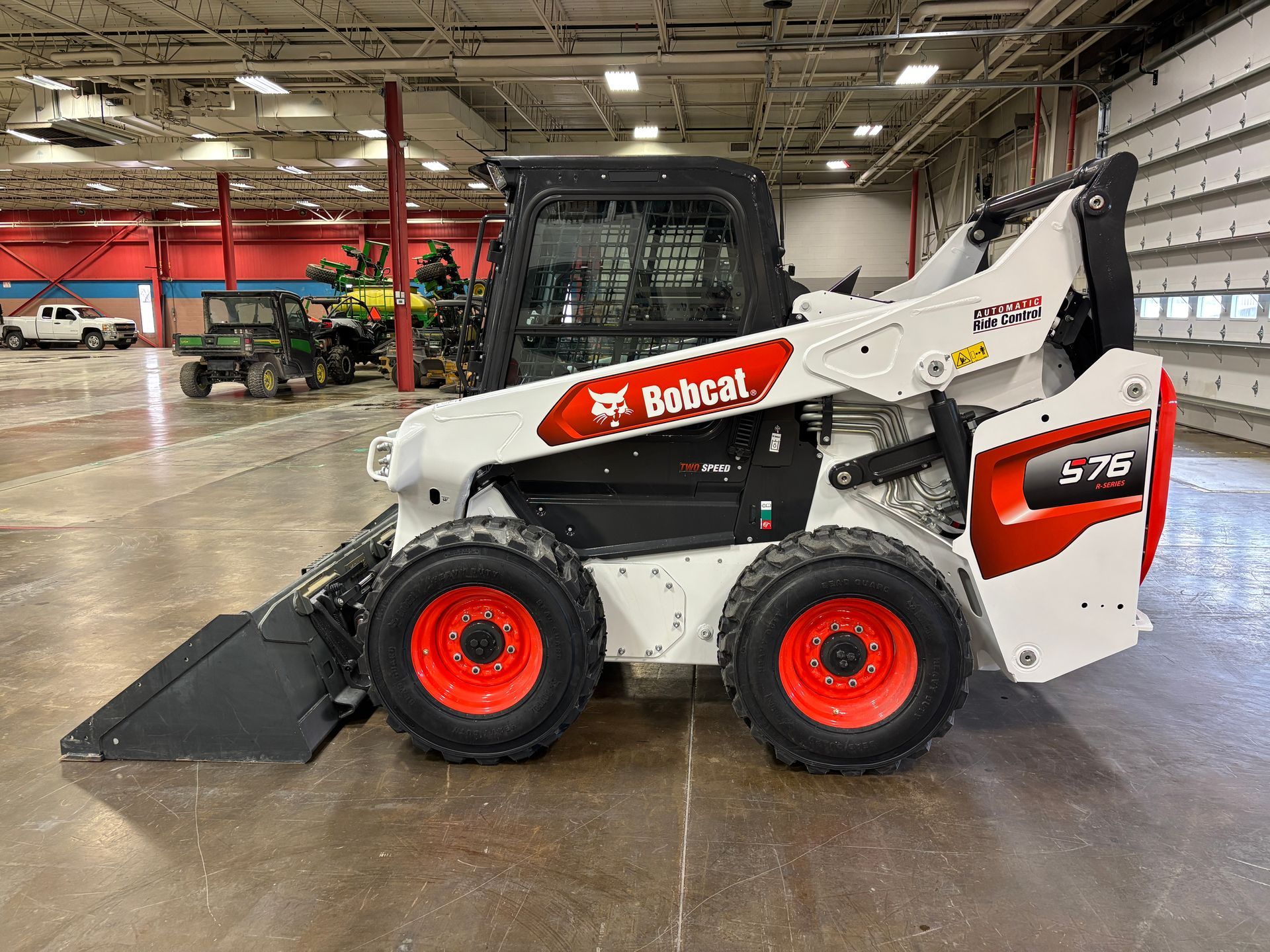 White Bobcat S76 skid-steer loader with a bucket in an indoor garage.