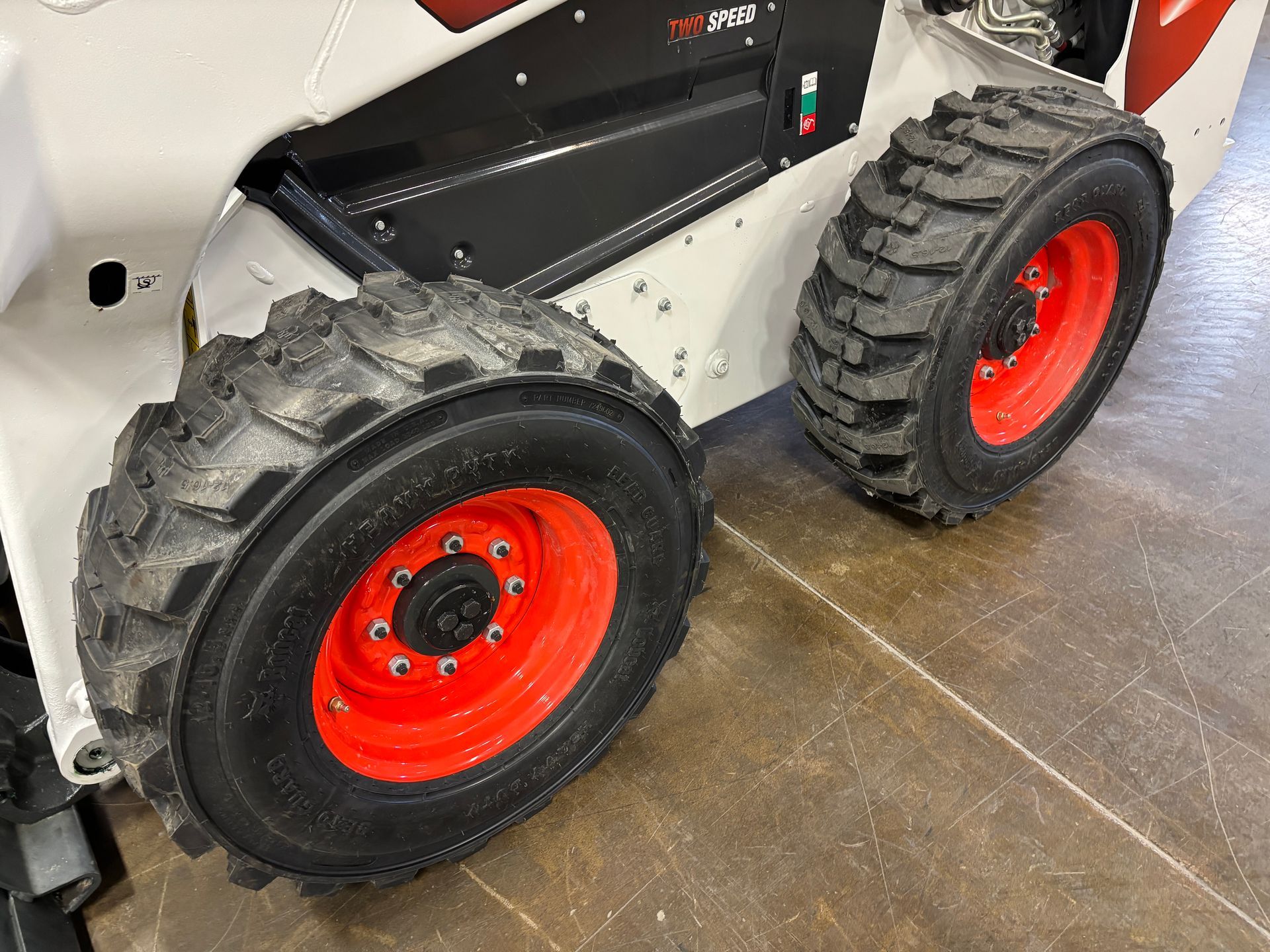 Close-up of a white and black skid steer loader with two large black tires on red rims.