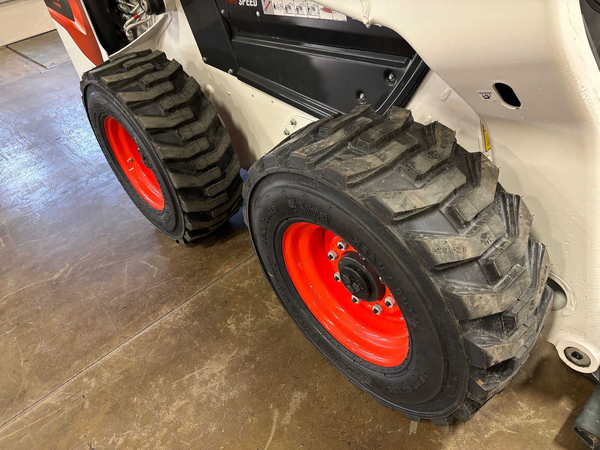 Close-up of Bobcat skid-steer loader's tires. The red wheels have black rubber tires on a light-colored machine.