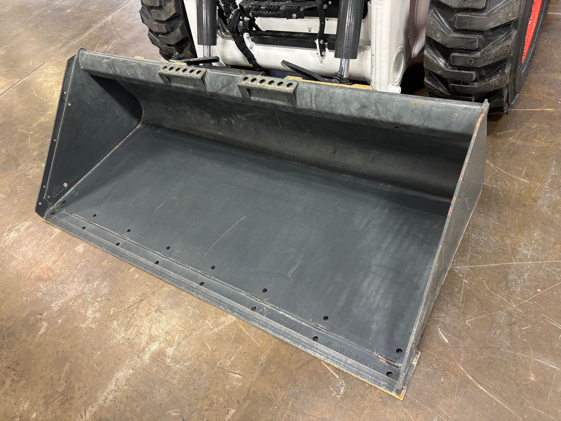 Bobcat loader bucket, gray steel, on a concrete floor.