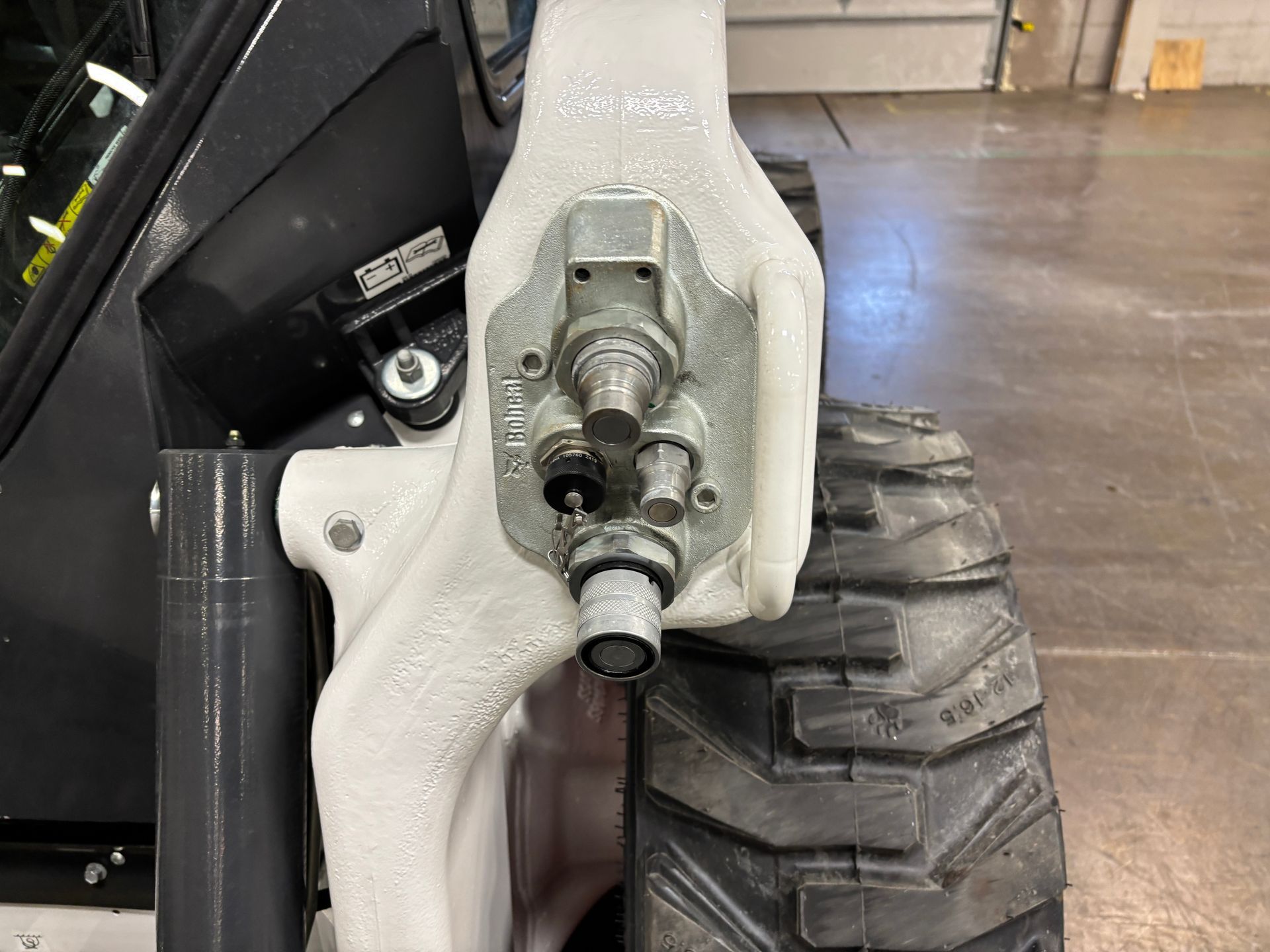 Close-up of a white skid steer arm with hydraulic fittings and a tire.
