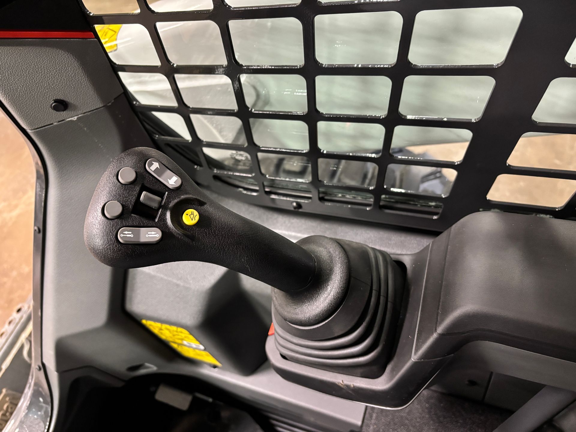 Joystick control inside a skid steer cab, with multiple buttons, a protective grate behind.