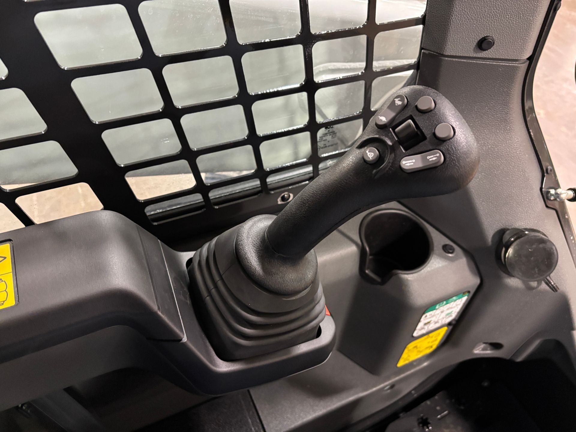 Black joystick control panel inside a vehicle cab with cup holder and safety cage.