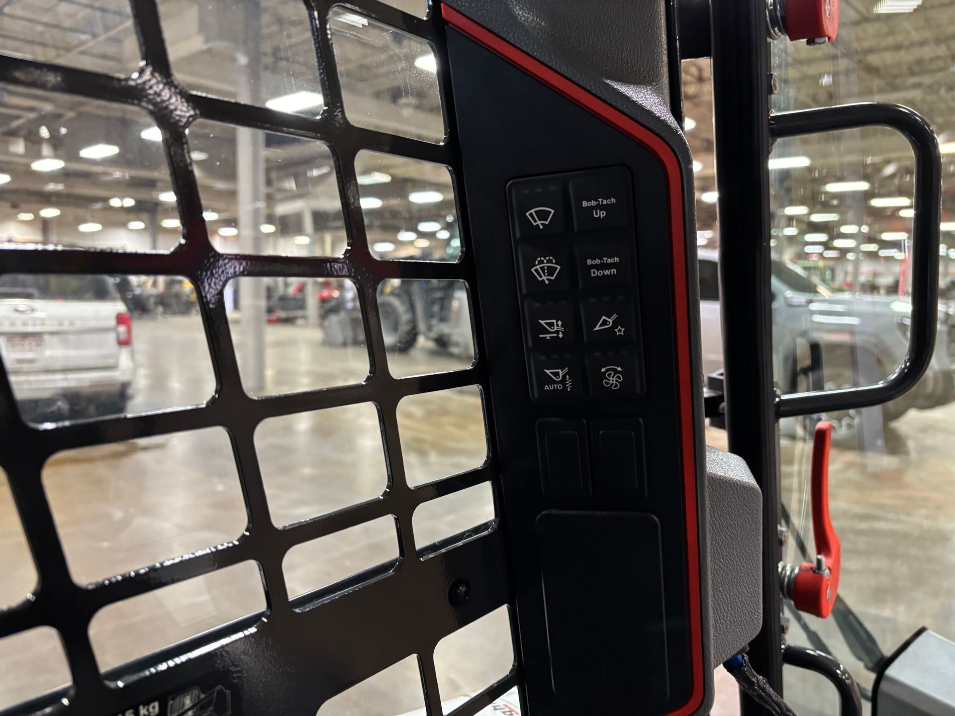 Black control panel on a skid steer cage with red accents and various button icons.