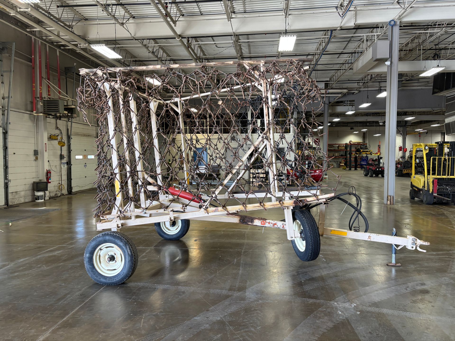 White utility trailer with metal cage covered in camouflage netting, indoors.