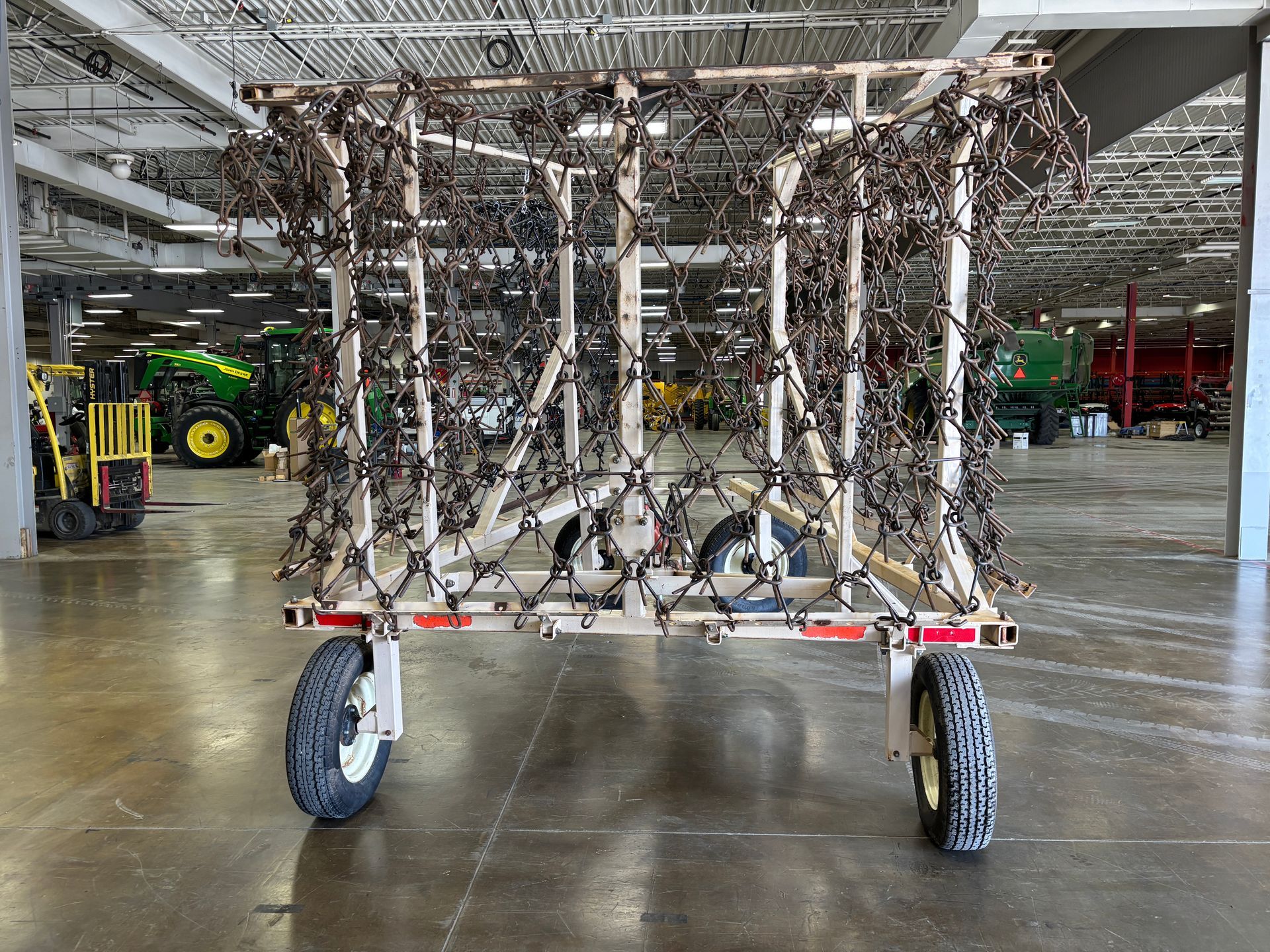 Agricultural harrow with spiked chains mounted on a wheeled frame inside a warehouse.