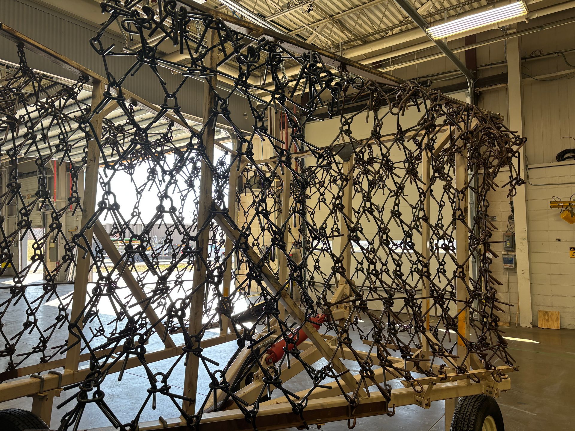 A wooden cart with a dark chain-link mesh structure attached, inside a warehouse.