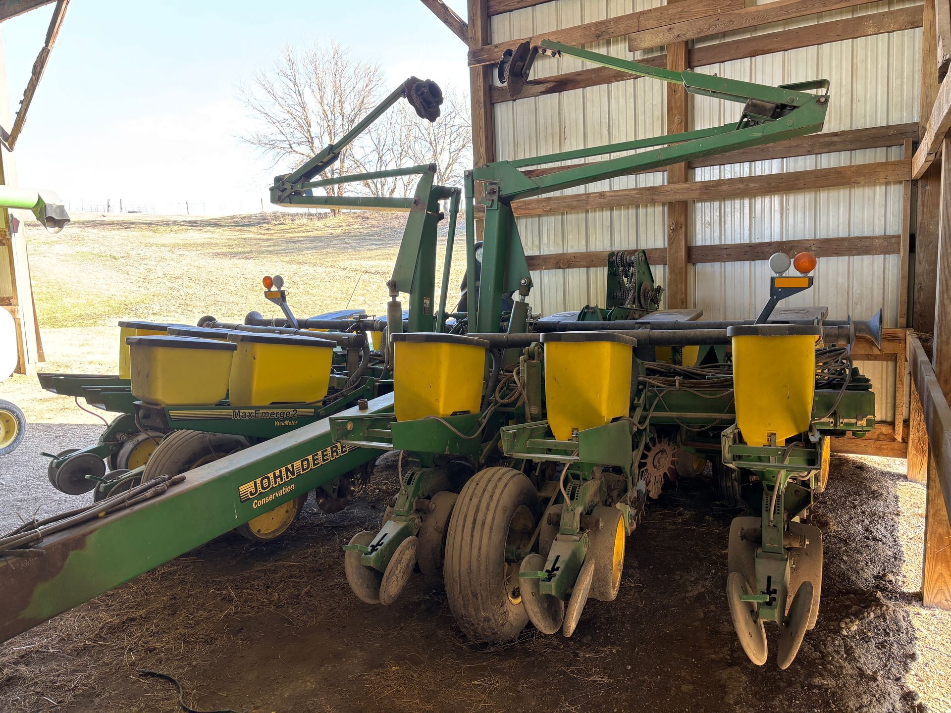 John Deere Superflex planter machine in a barn, yellow seed hoppers, green arms, tires.