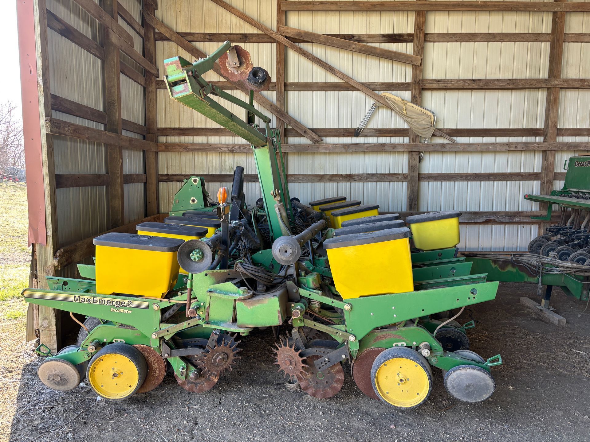 Green John Deere planter machine inside a wooden shed.
