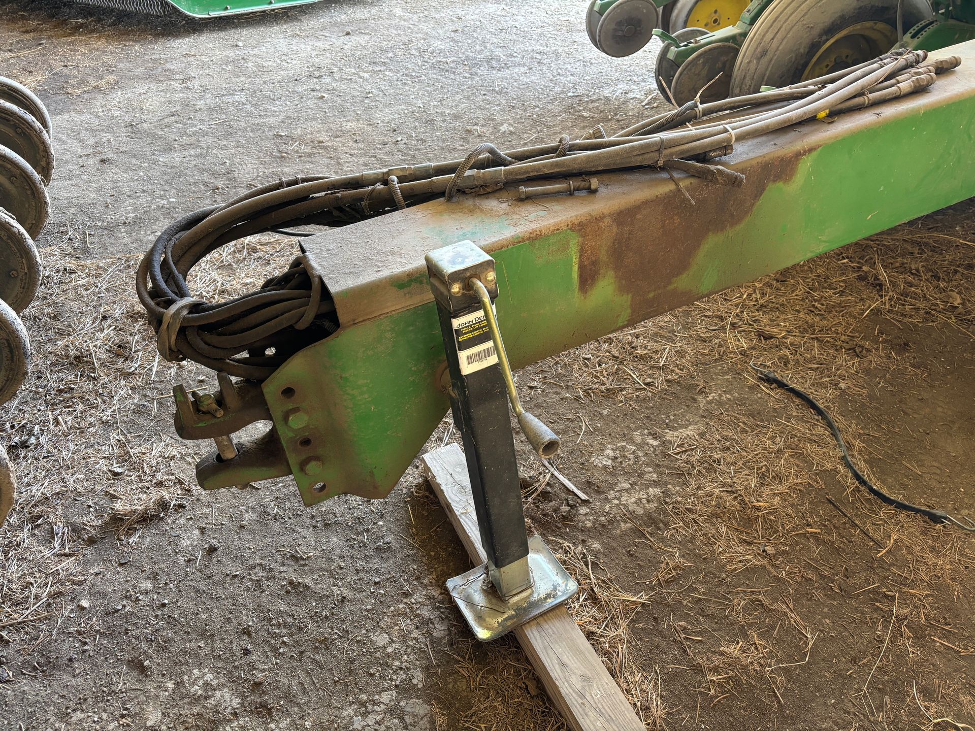 Green farm implement with a jack and hoses, in a barn.