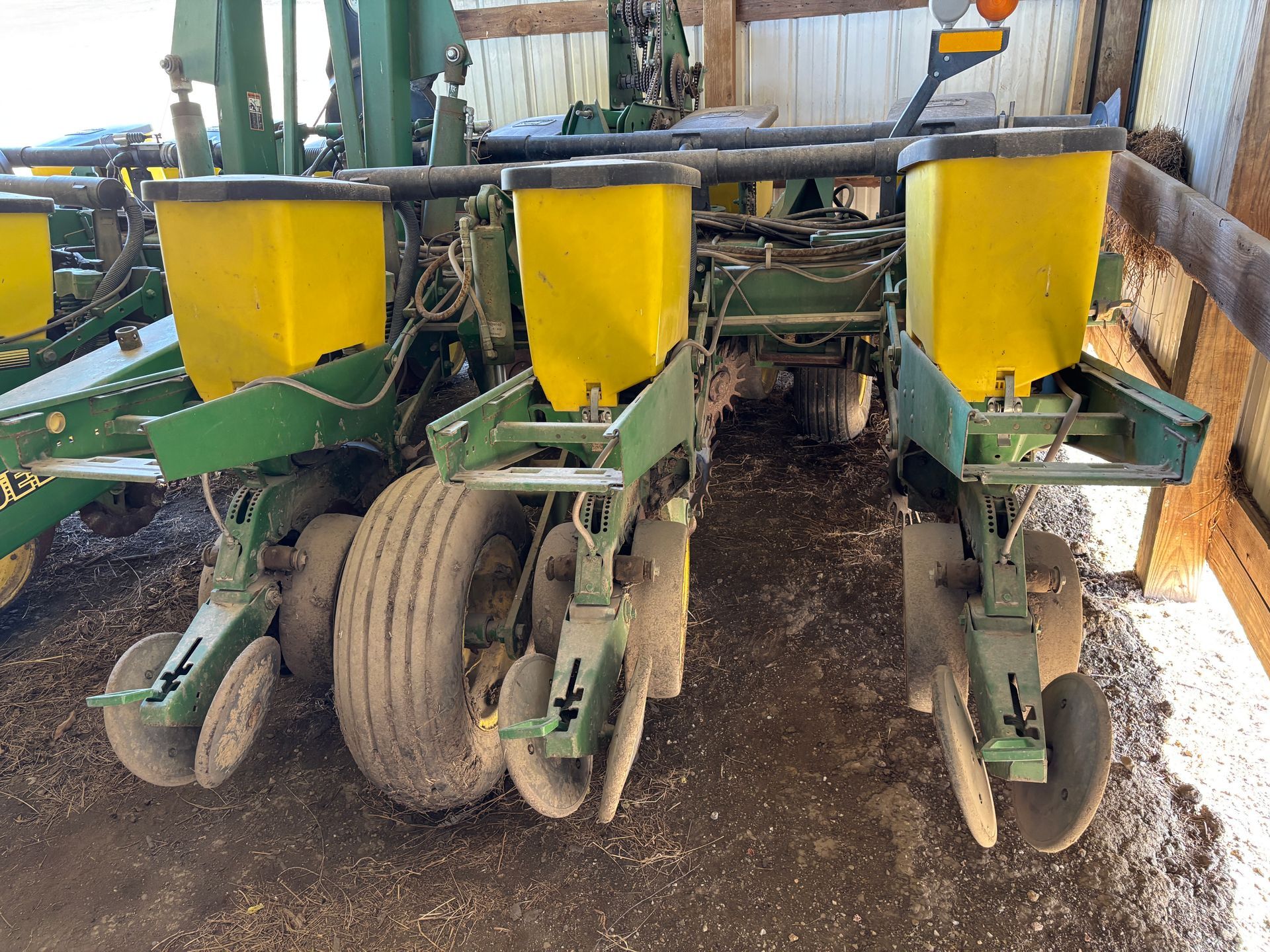 John Deere corn planter with three yellow seed hoppers, outdoors, dusty.