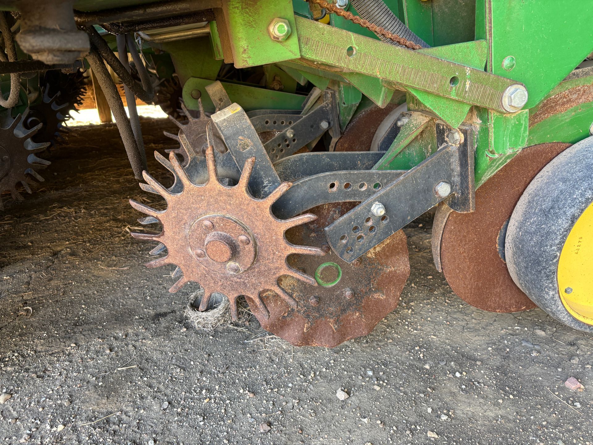 Close-up of a rusty, toothed disc blade on a green and yellow farm implement.