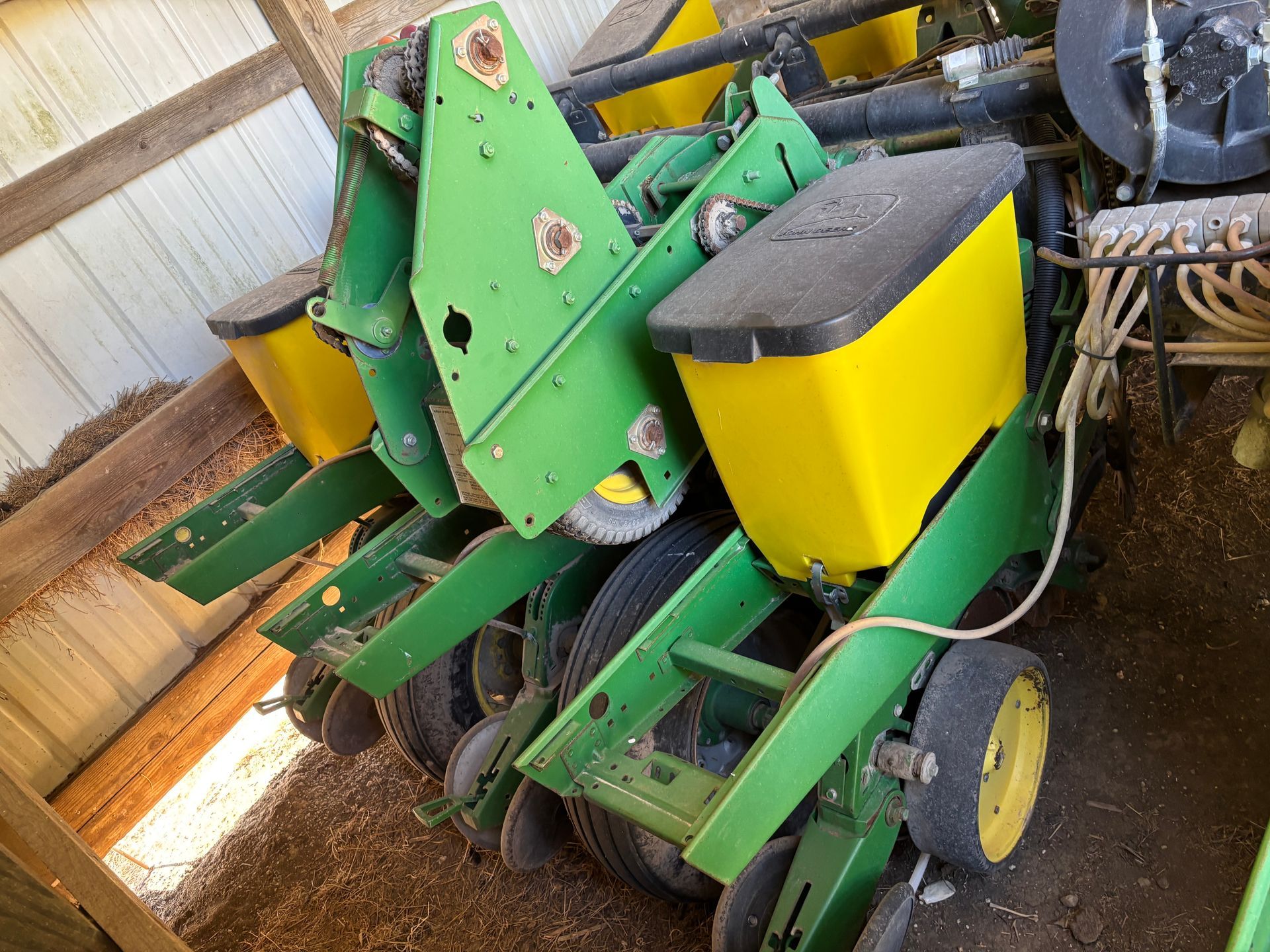 Green and yellow John Deere planter machine inside a wooden barn.