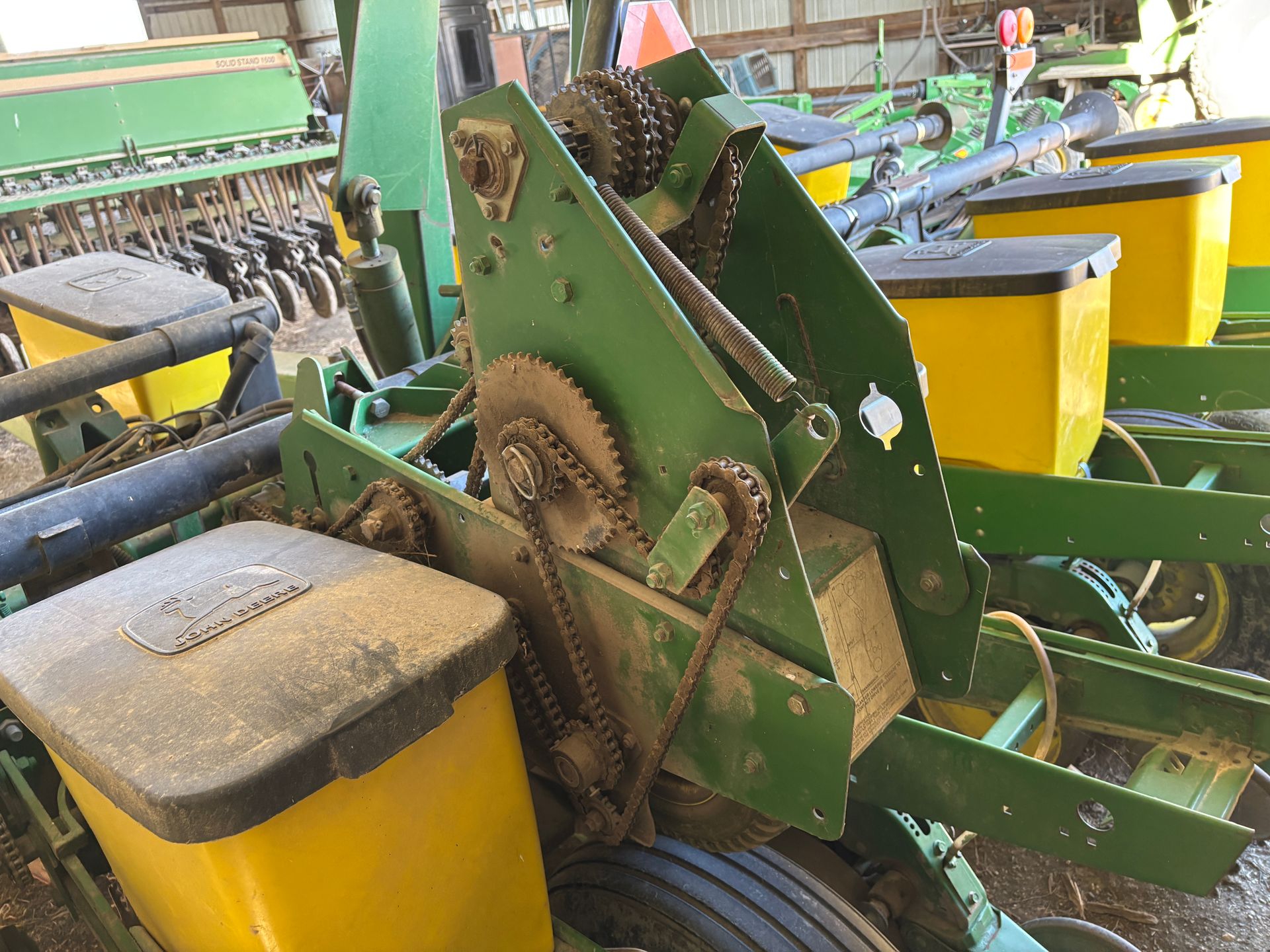 Green and yellow John Deere planter; close-up of gears, chains, and seed hoppers.