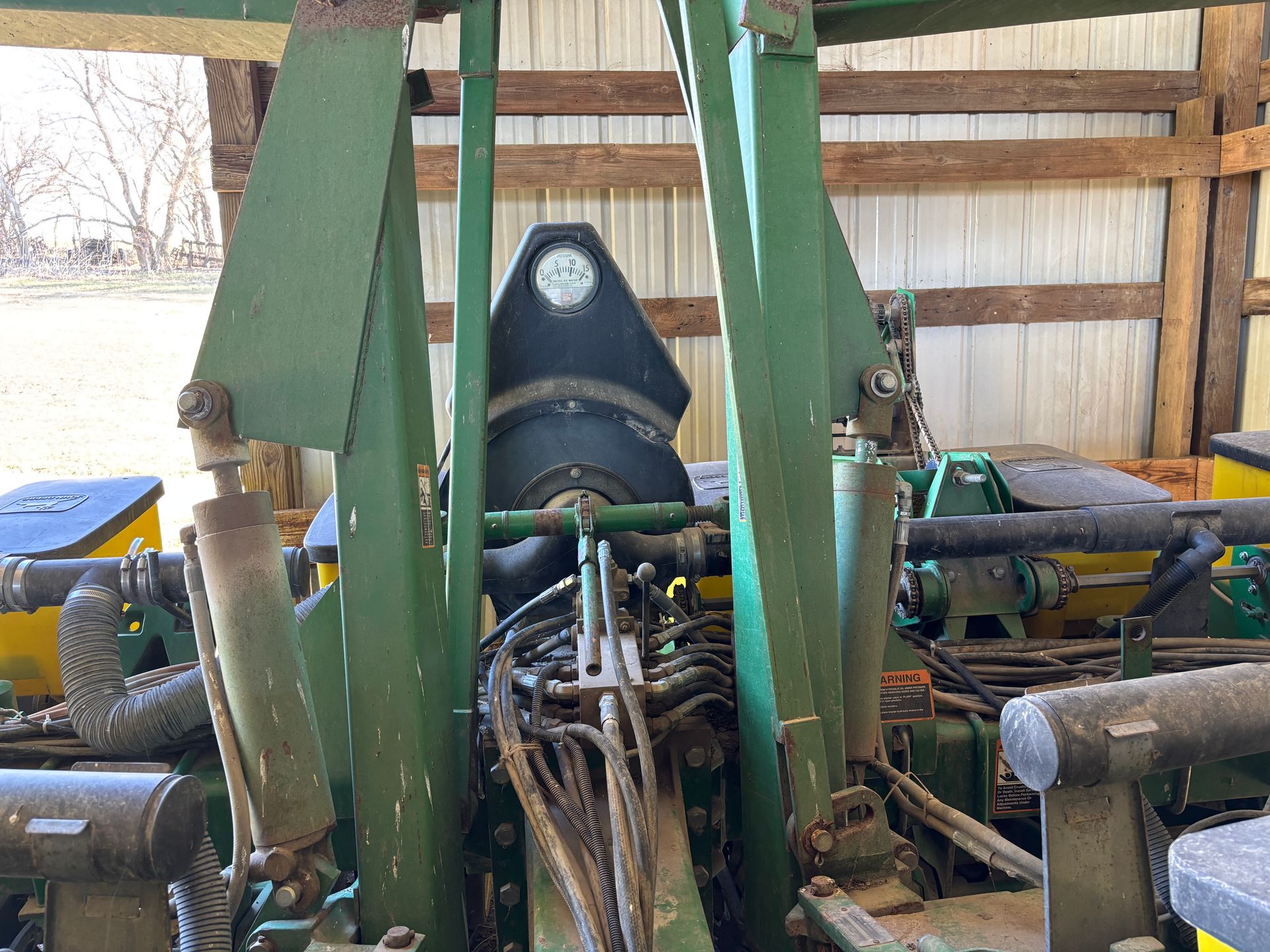 Green and black farm machinery with a gauge in a barn setting.
