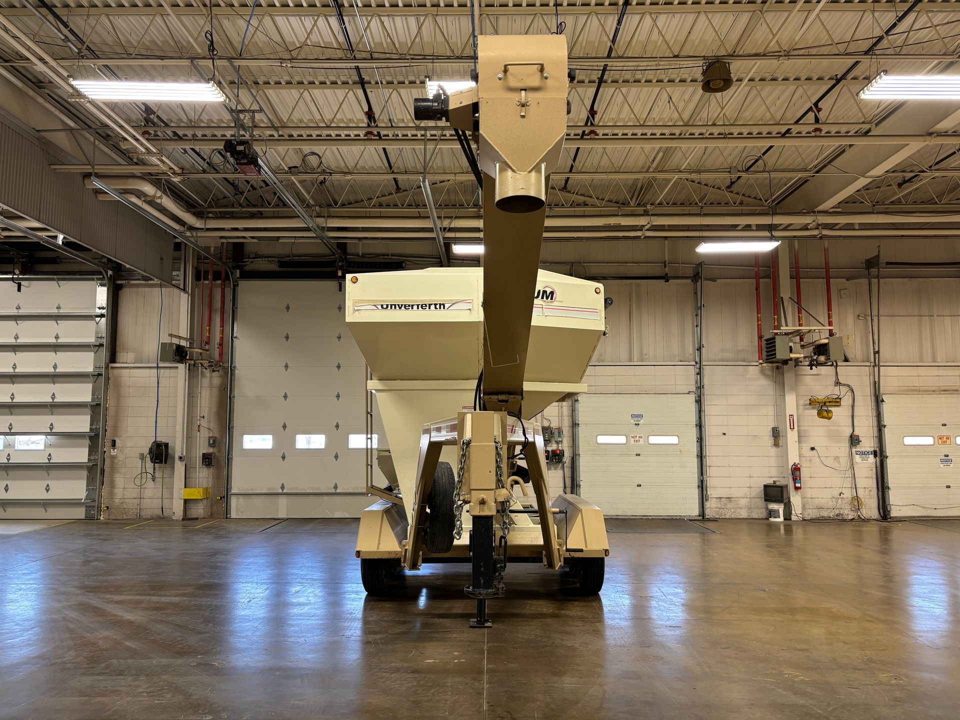 A tan grain conveyor with a screw auger in a large warehouse with white doors.