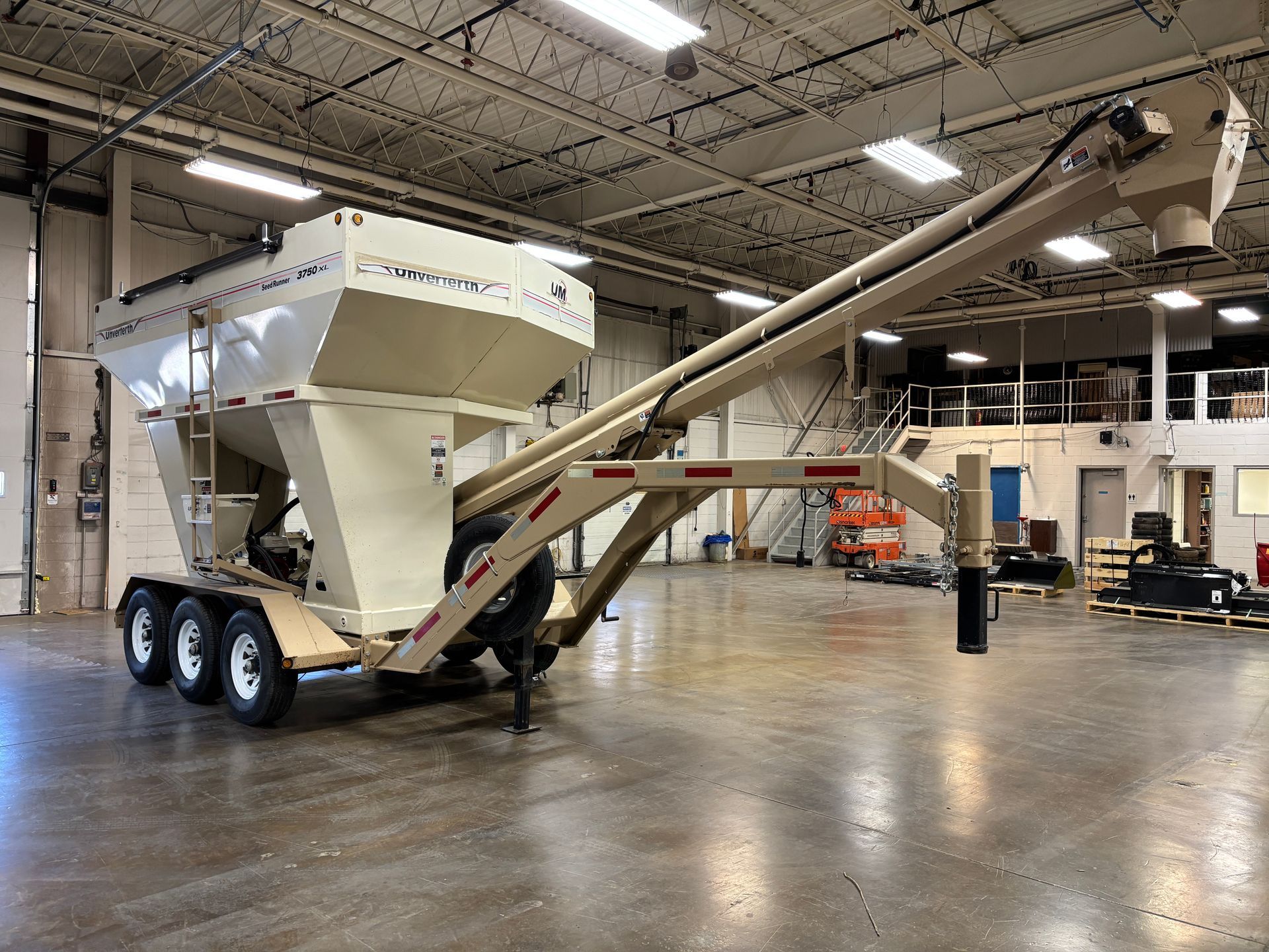 Beige grain cart with auger, parked in a warehouse.