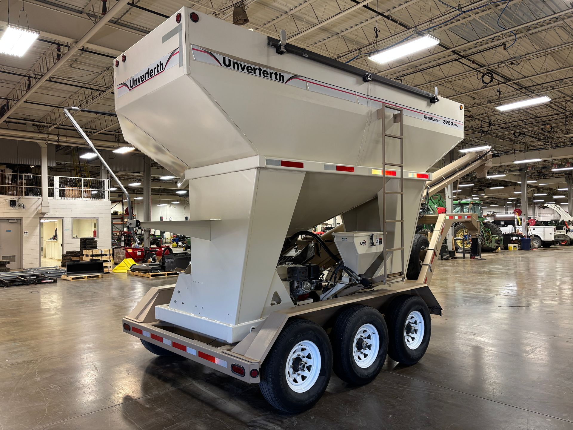 White and tan UWRIGHT seed tender trailer with three wheels, indoors.