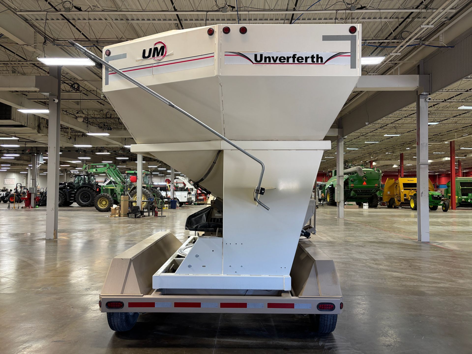 White Umverferth fertilizer spreader trailer, indoors, with farm equipment in background.