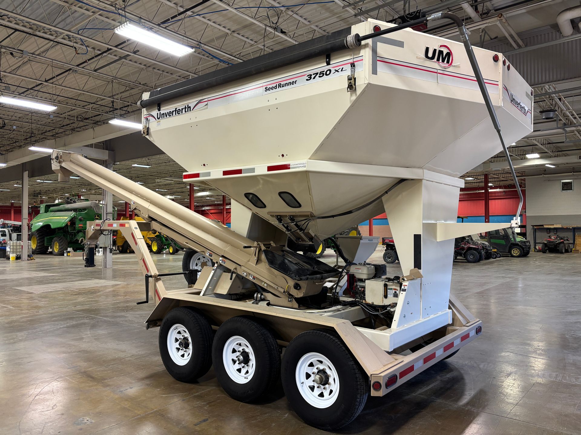 Tan and white agricultural seed tender trailer with three wheels, indoors.