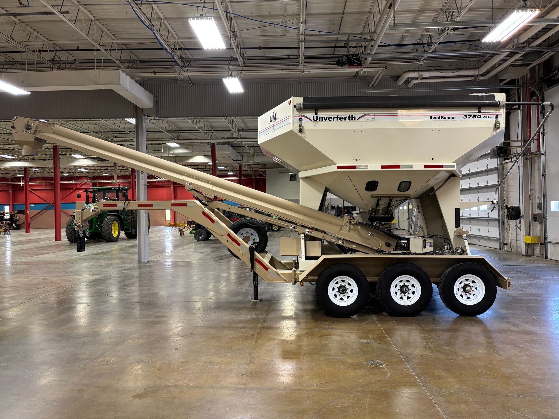 Beige grain cart with augers, parked in a warehouse.