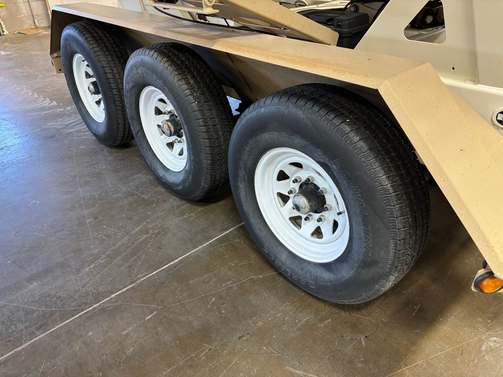 Three tires with white rims on a trailer, angled on a concrete floor.