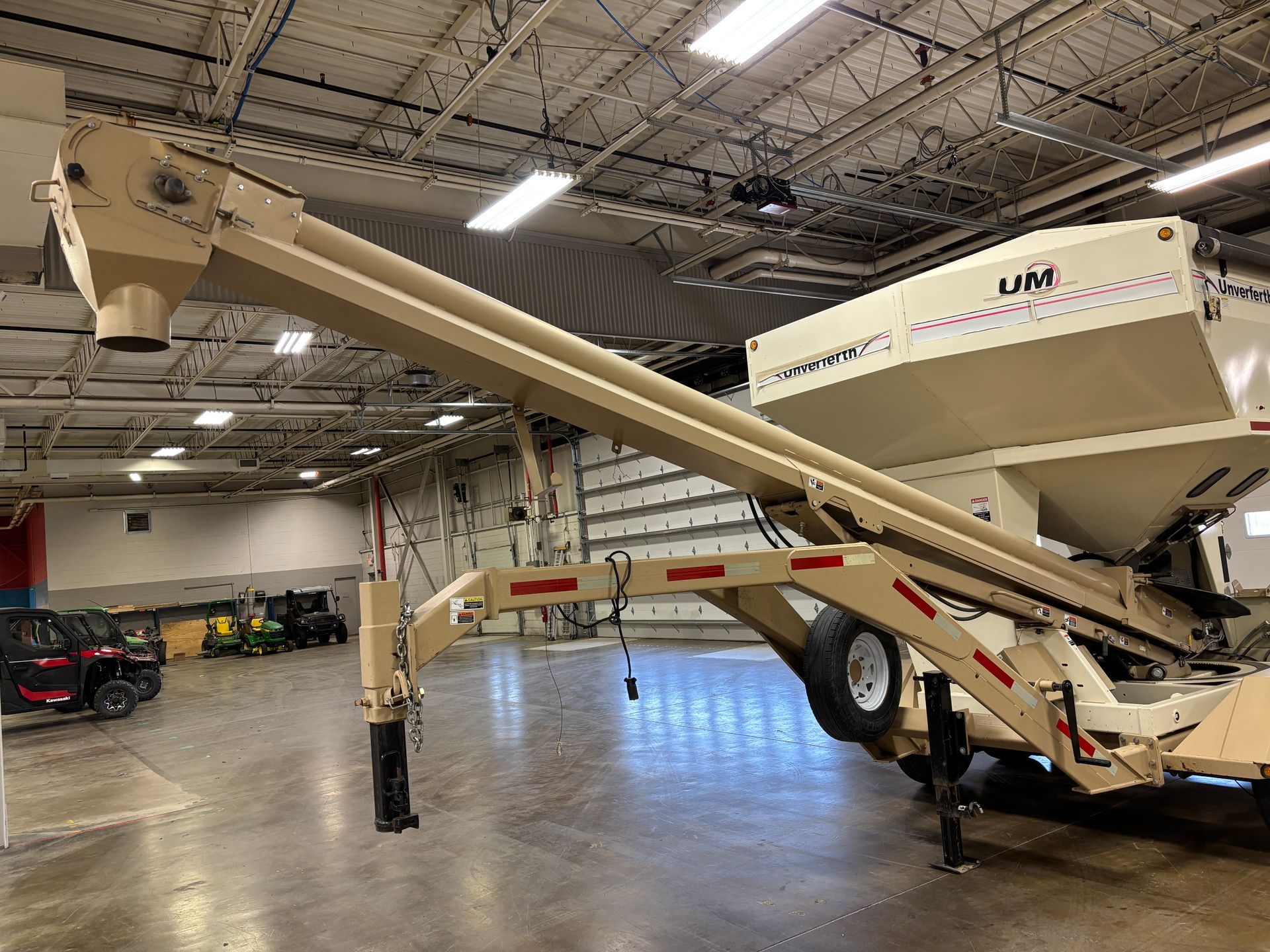 A beige grain auger on a trailer is in a large indoor space.