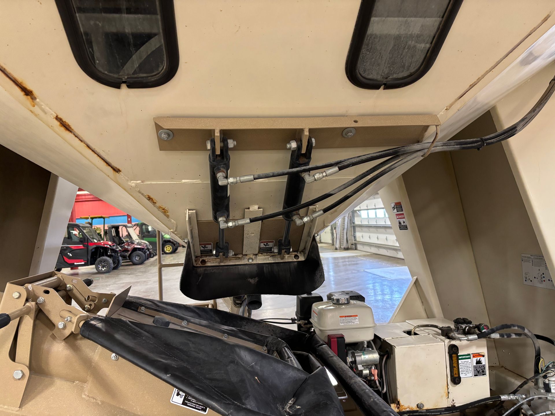 Interior view of a beige industrial machine. Hydraulic lift mechanism and small engine visible.