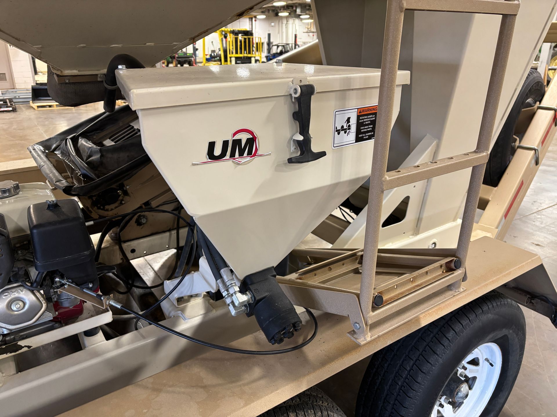 A beige UM equipment trailer with a hopper, engine, and a black tire.