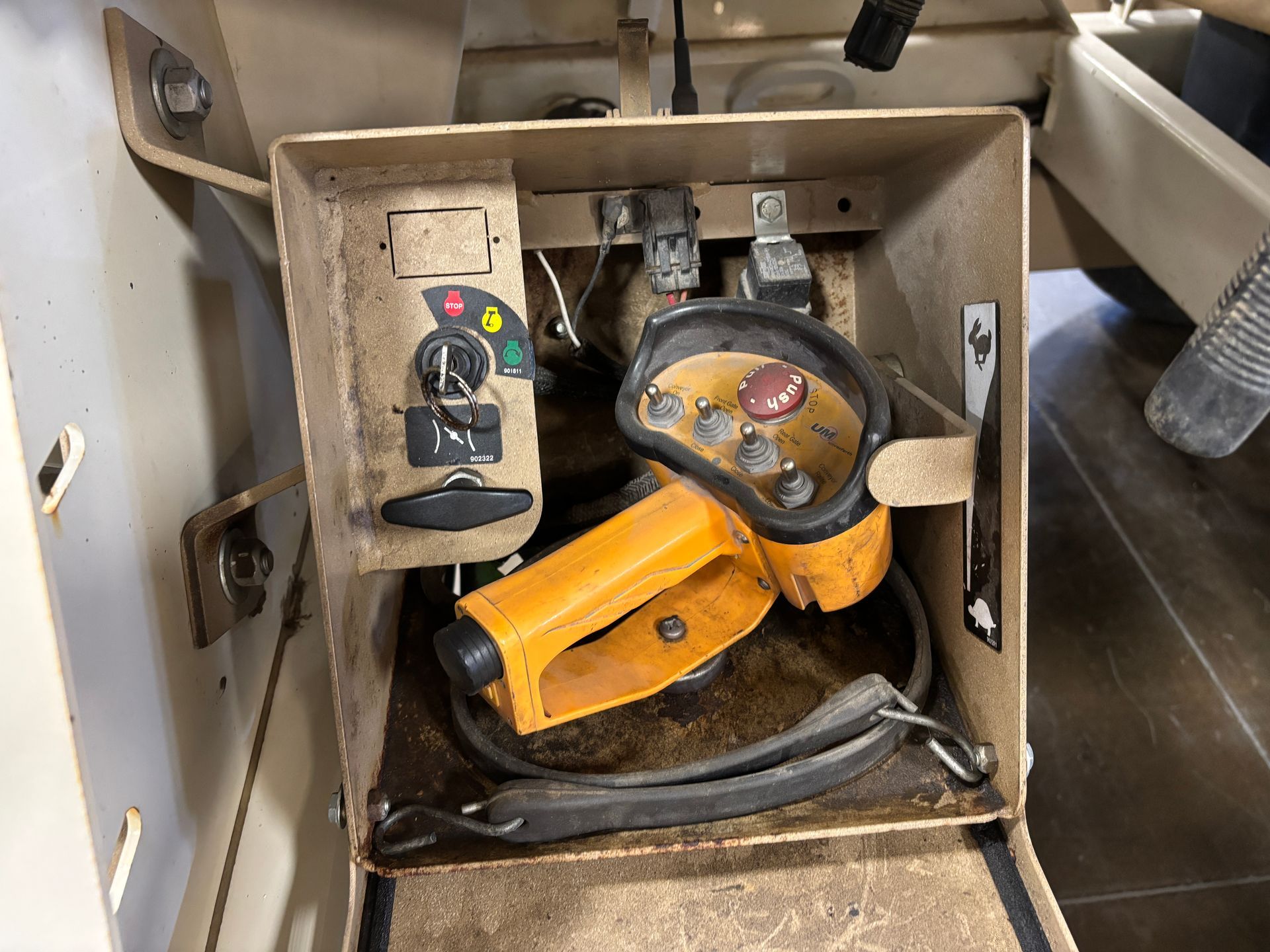 Control panel and remote inside a machine's cabinet. Yellow and black controls, dials, and a handle.