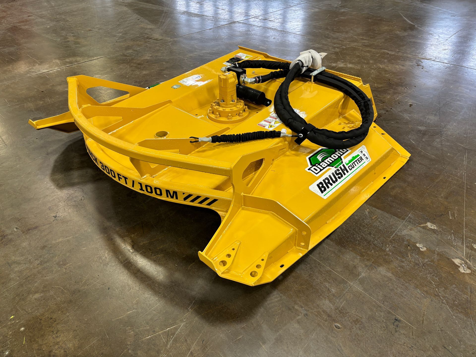 Yellow brush cutter on a gray floor; has black hoses and a rounded front.