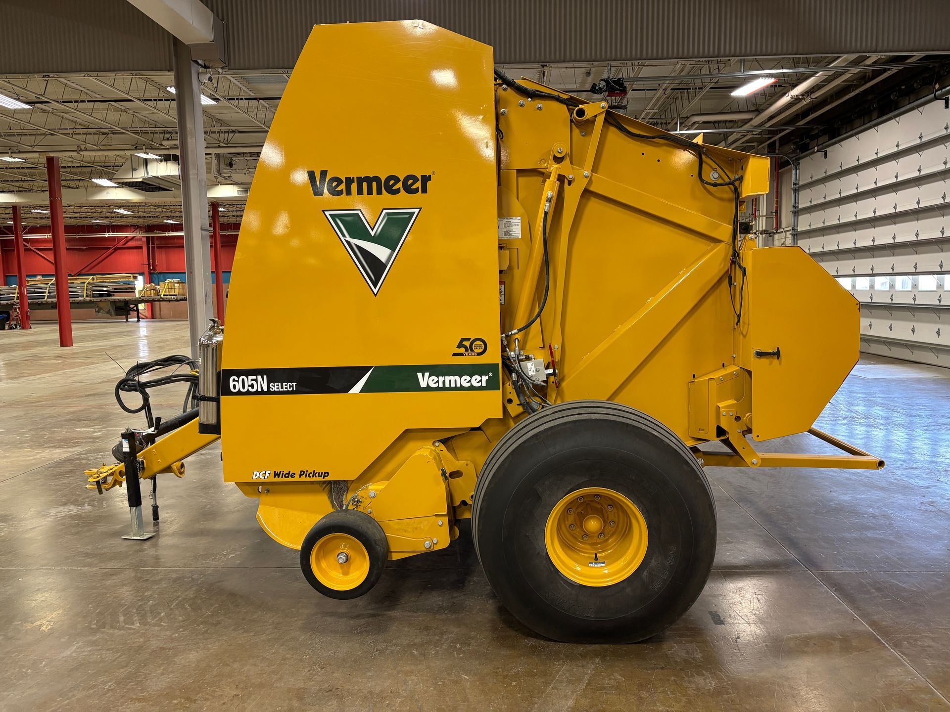 Yellow Vermeer round baler in an indoor setting, side view shot.