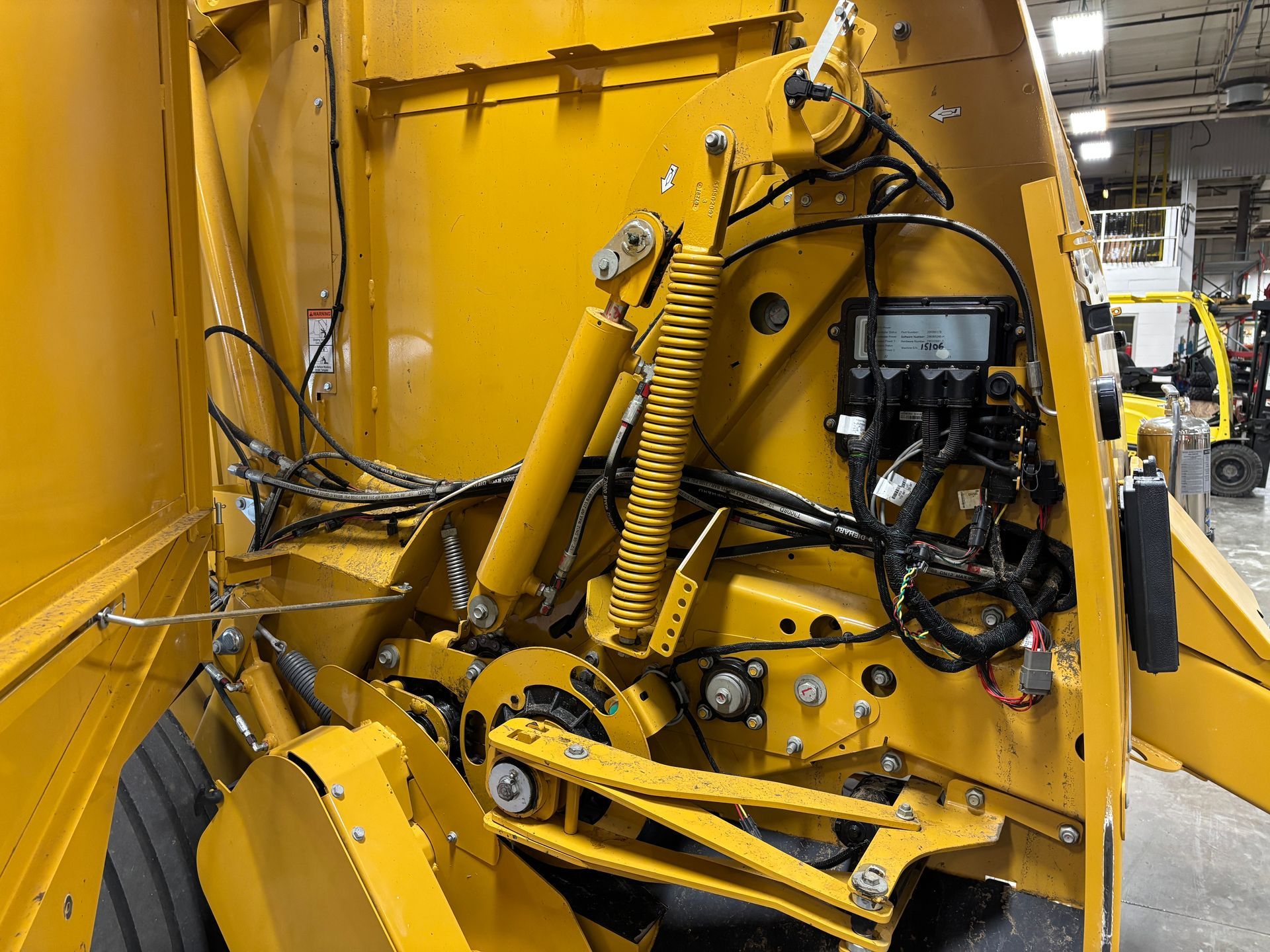 Yellow baler interior with belts, chains, and hydraulics.
