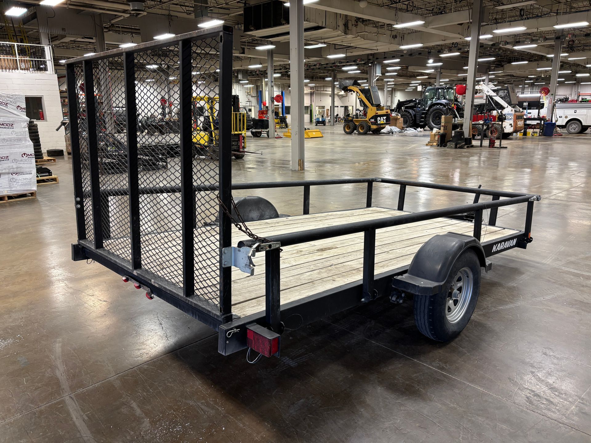 Black utility trailer with mesh sides and wood bed, parked indoors.