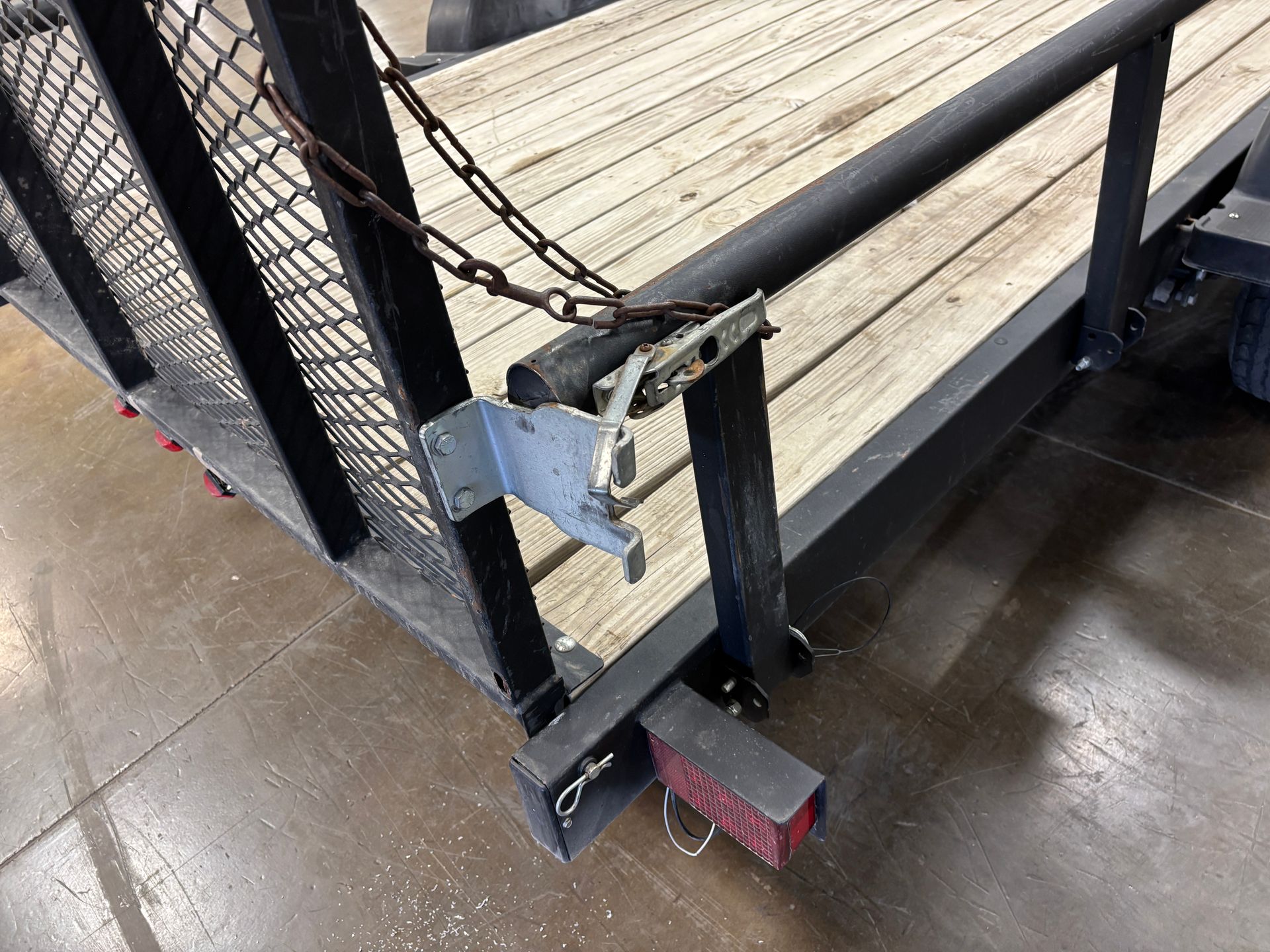 Trailer's rear corner detail: metal frame, wooden deck, safety chain, taillight, and securing latch.